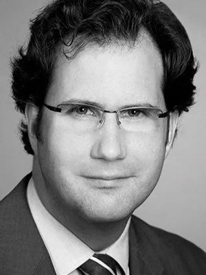 Schwarz-weiß Porträt eines Mannes mit dunklen, gewellten Haaren und Brille