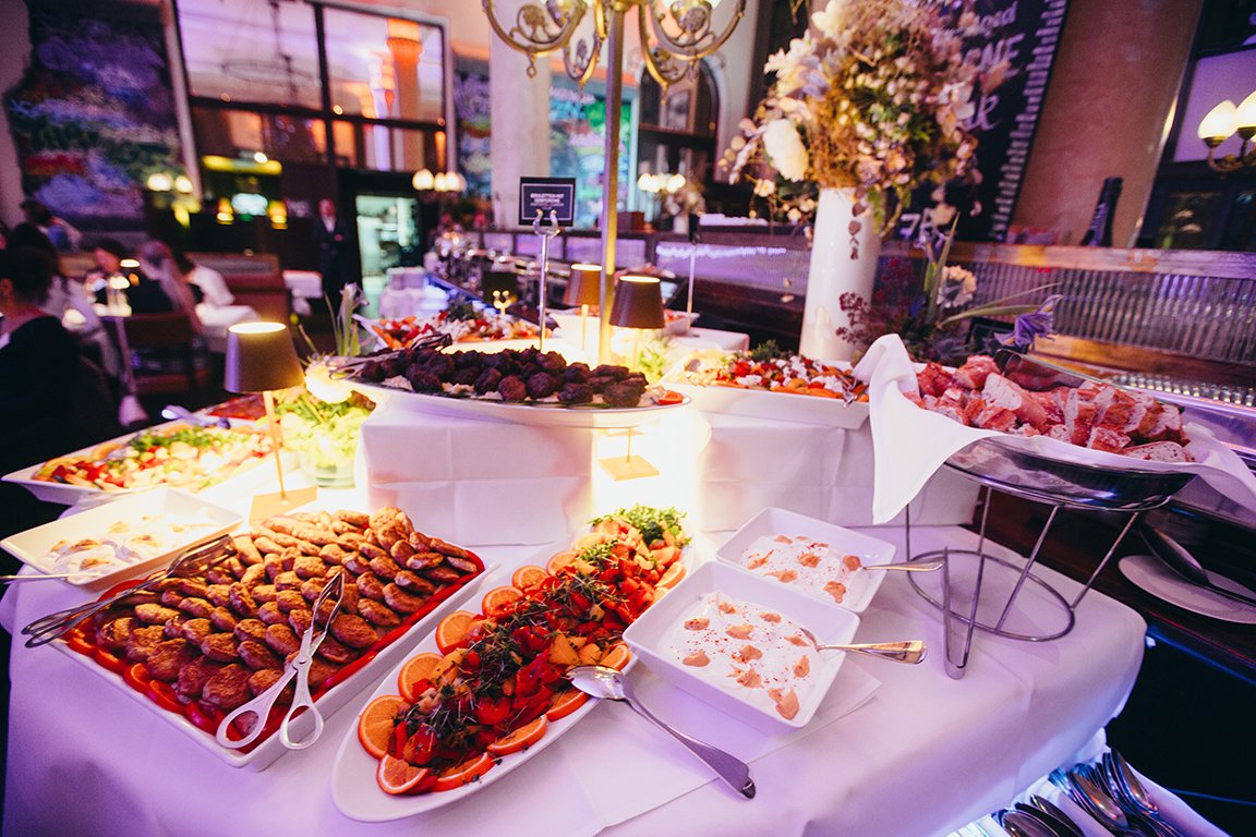Buffet mit verschiedenen warmen und kalten Speisen, darunter Fleischbällchen, Gemüse, Salate und Desserts, in einem festlich dekorierten Raum mit Blumen und warmem Licht.