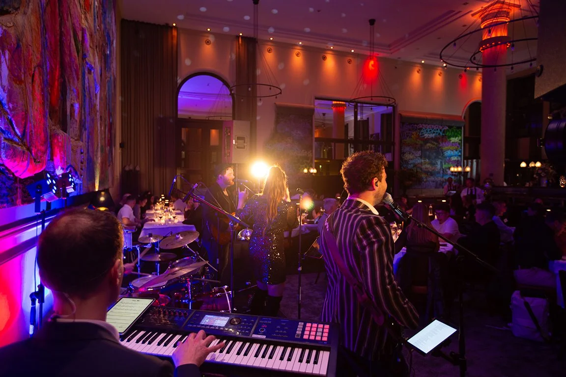 Live-Musikperformance in einem eleganten Restaurant mit einem Pianisten, Saxophonisten, Sängerinnen und Publikum im Hintergrund.
