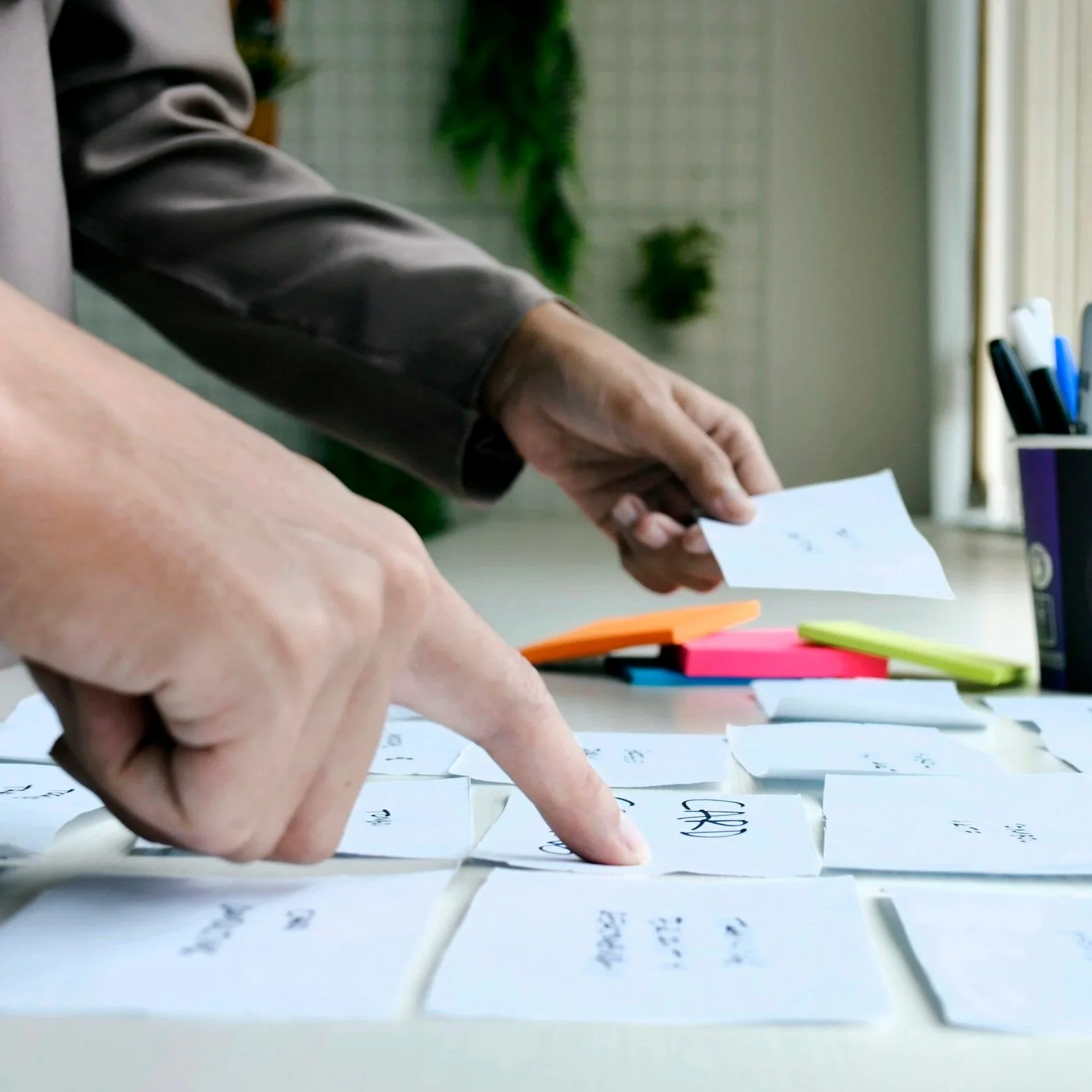 People sorting or organizing flashcards or notes on a table, with colorful sticky notes and writing materials nearby.
