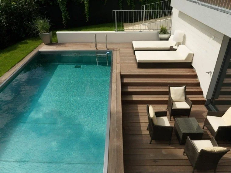 A backyard patio with a swimming pool, wooden deck, outdoor lounge chairs, and patio furniture.