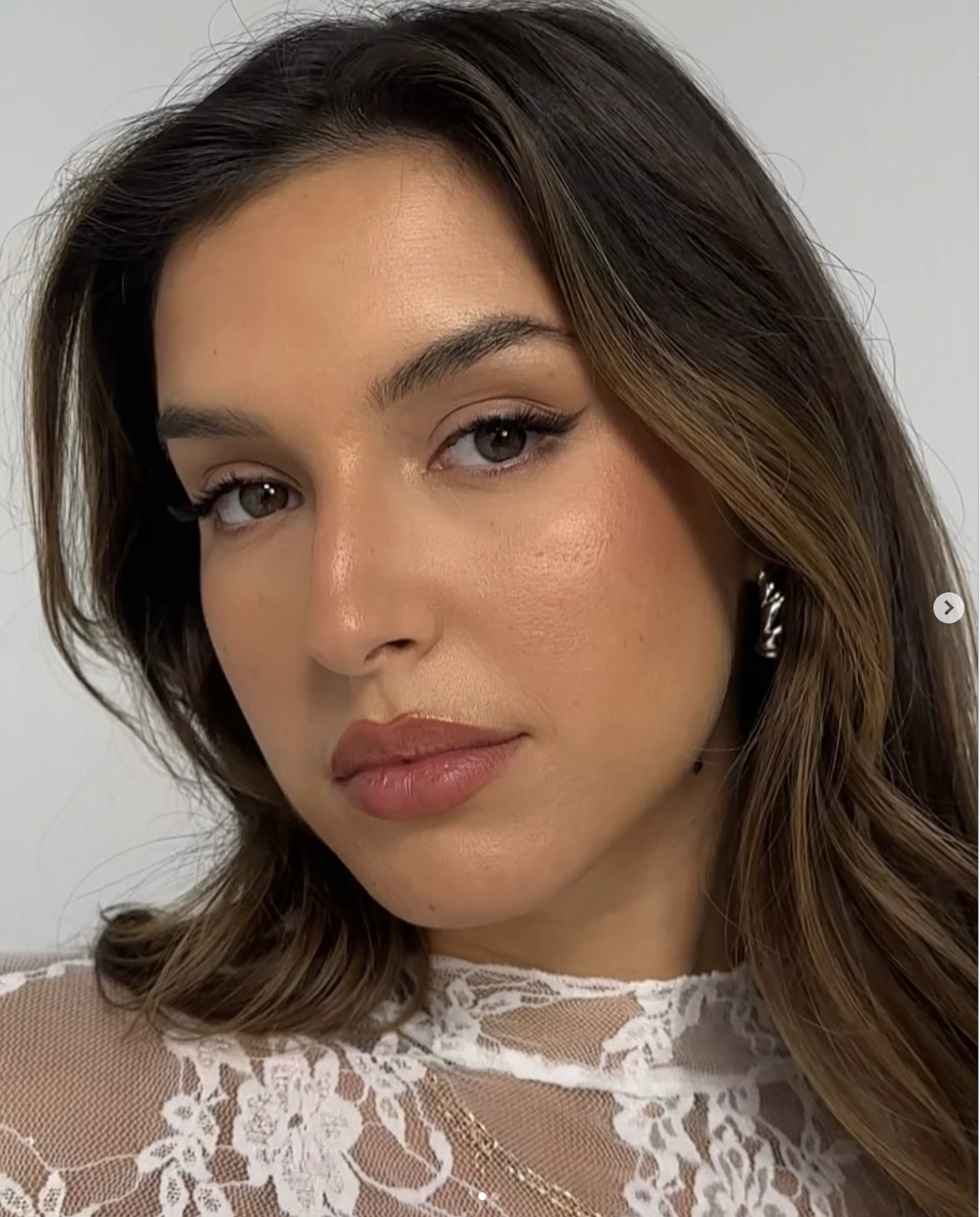 A close-up photo of a woman's face showing her eyes, nose, and lips. She has brown hair with blonde highlights, wearing subtle makeup, and a white lace top.