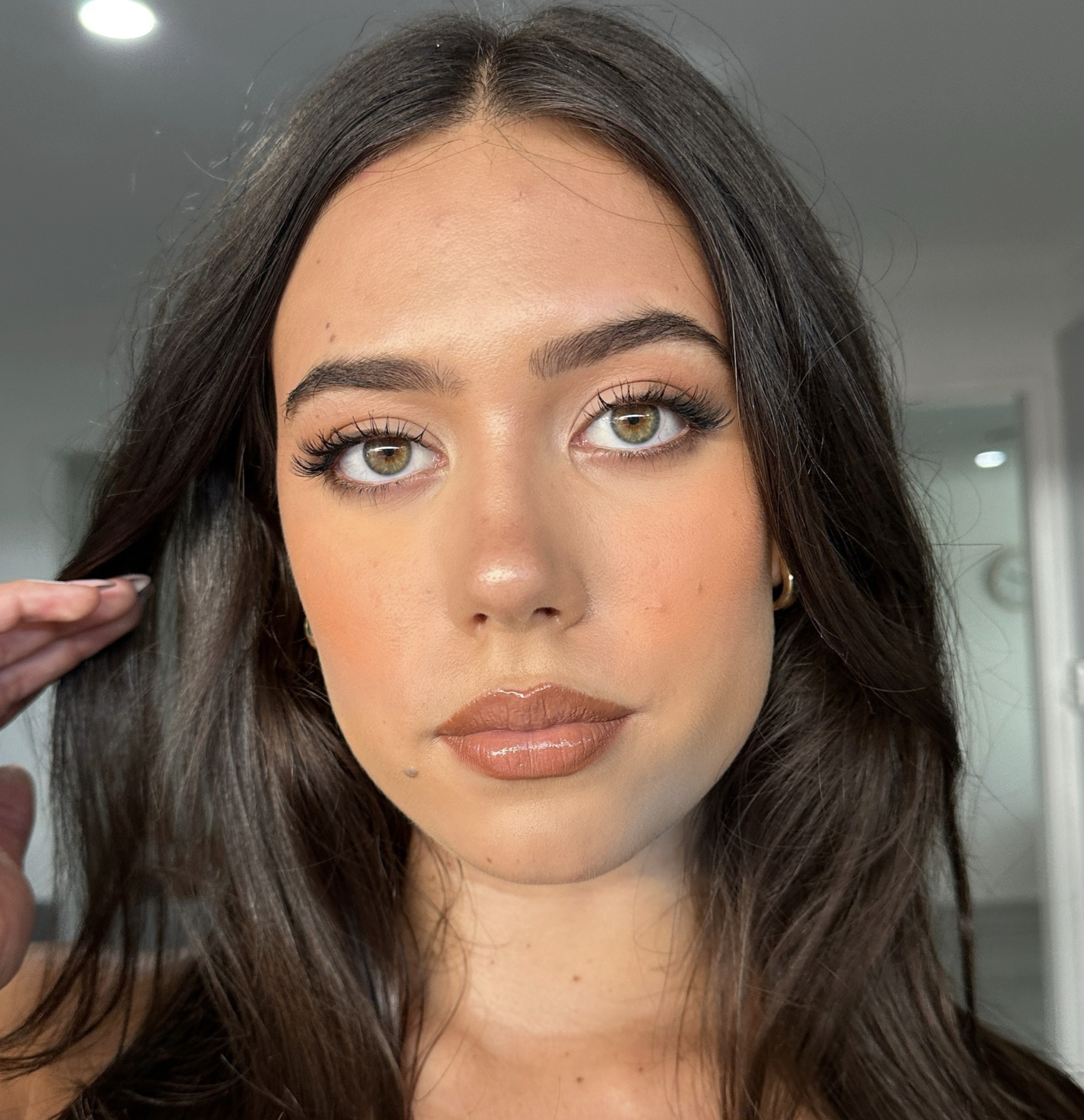 A woman with brown hair and hazel eyes, wearing makeup, with a neutral facial expression.