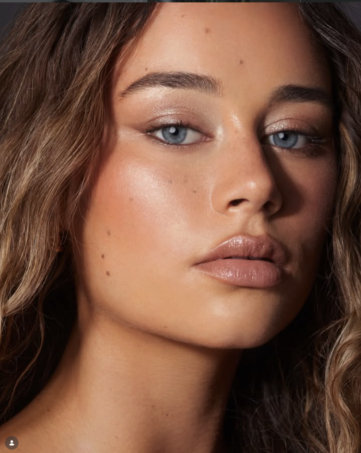 Close-up of a woman's face showing her blue eyes, brown hair, light makeup, and natural skin with some freckles.