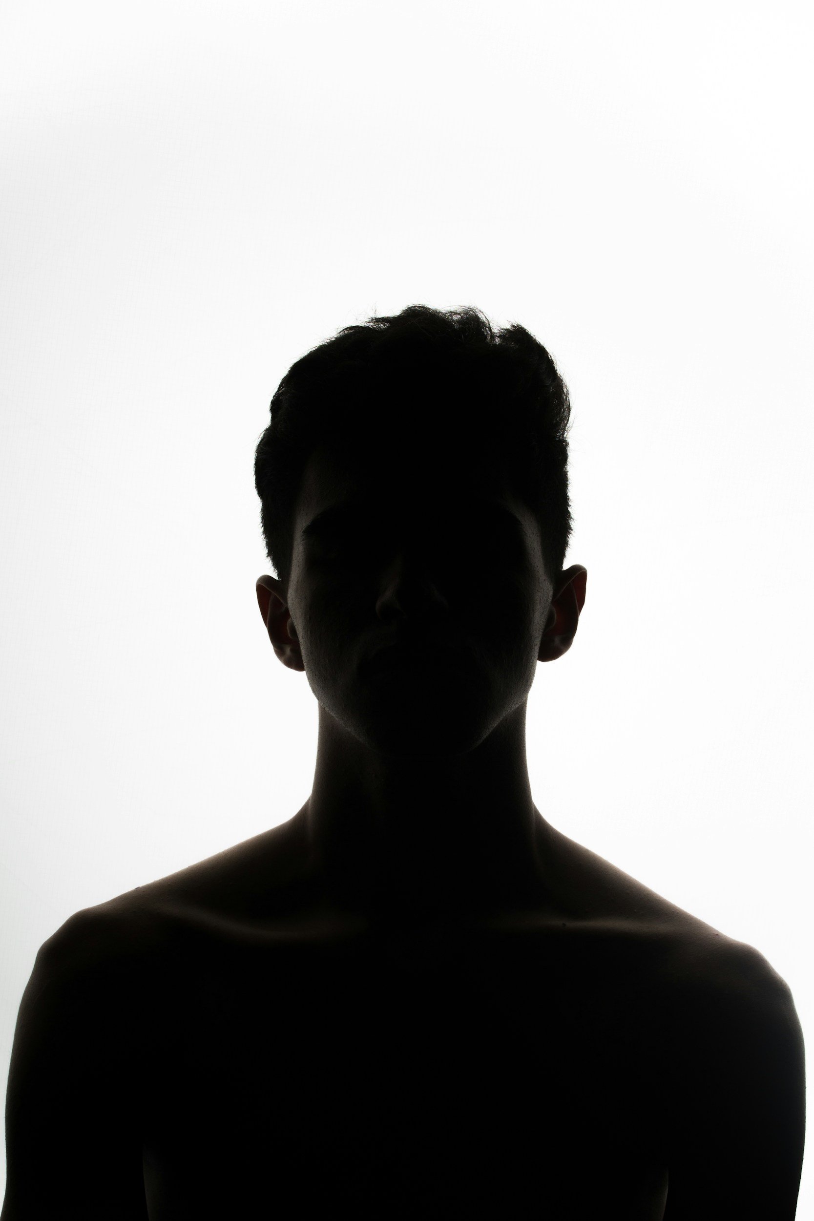 Silhouette of a person with short, curly hair against a bright white background, with shadowed facial features and upper body visible.
