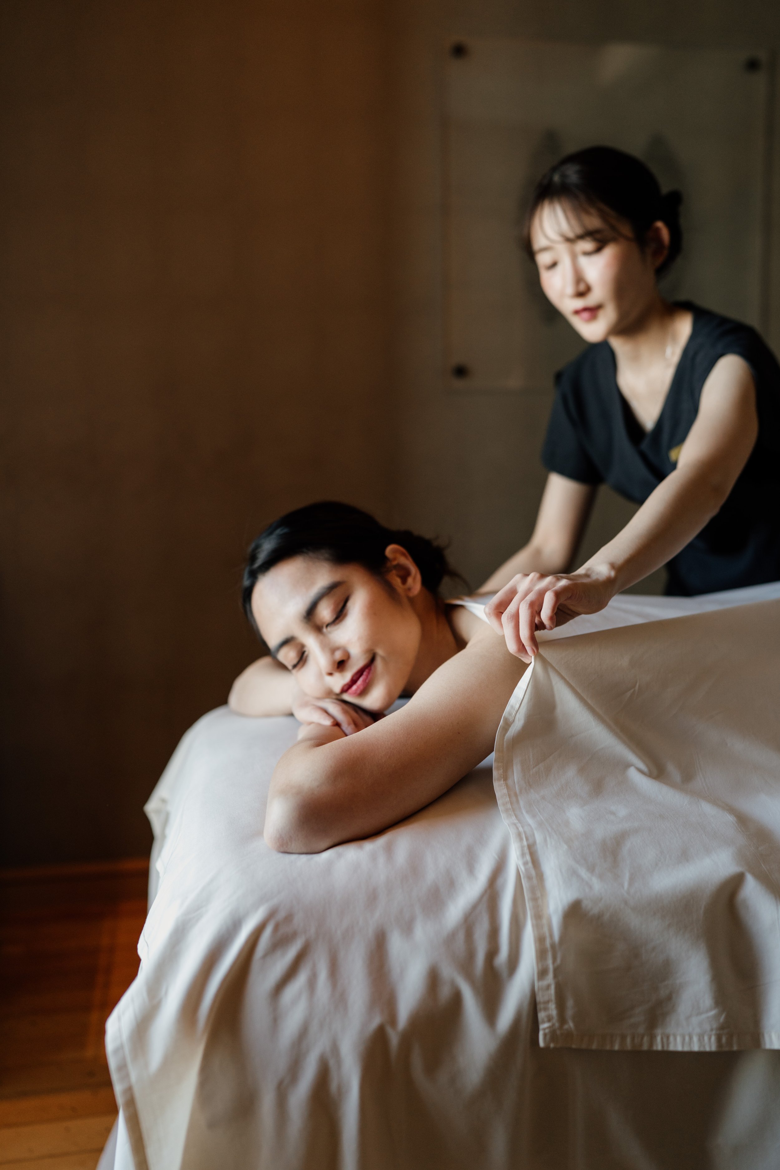 A guest is receiving a massage from a therapist in a spa room with dim lighting at The Ritz-Carlton, Tokyo. Editorial hospitality photography, Japan.  