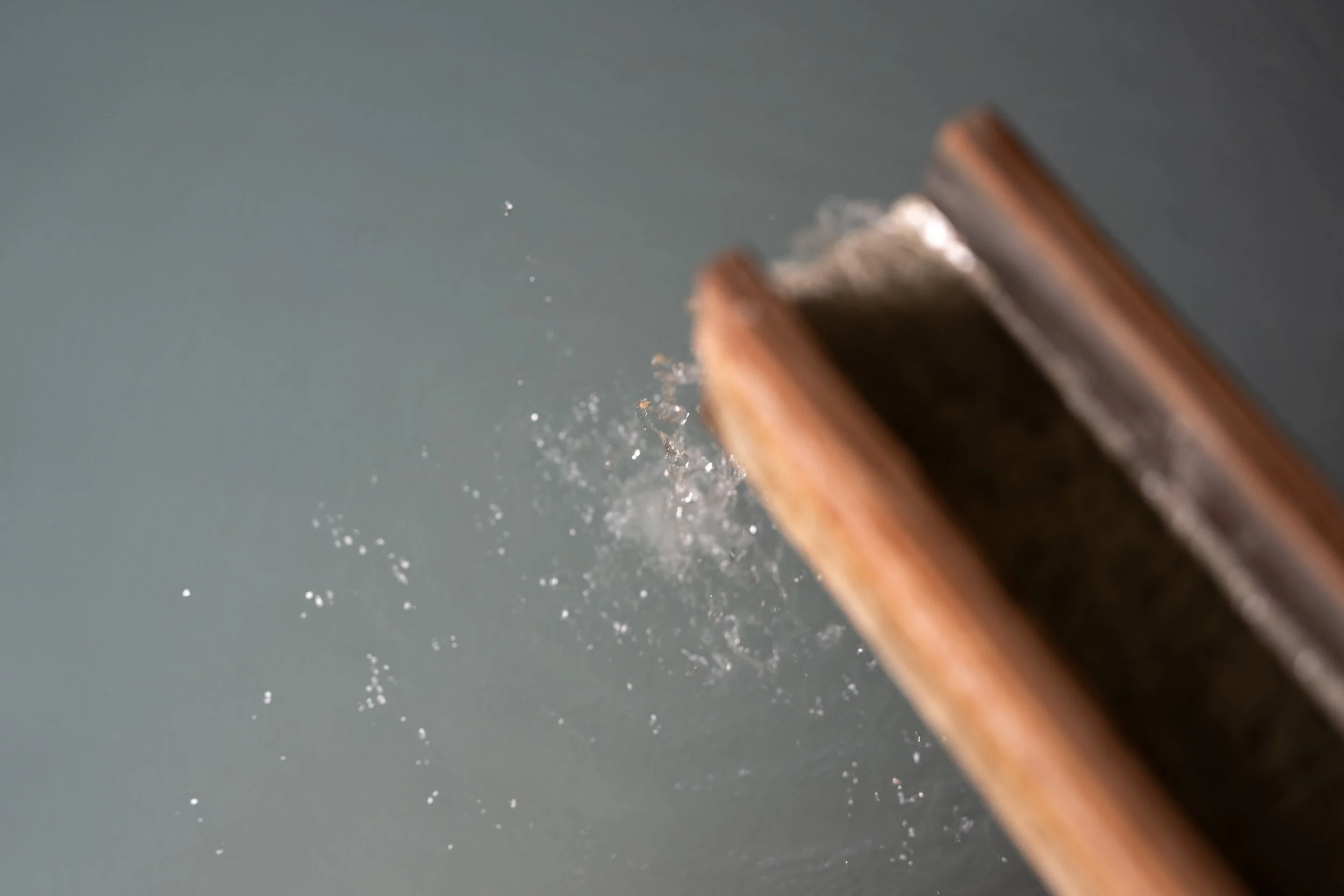 Close-up of a chisel striking a wooden surface, with wood dust and particles flying through the air.