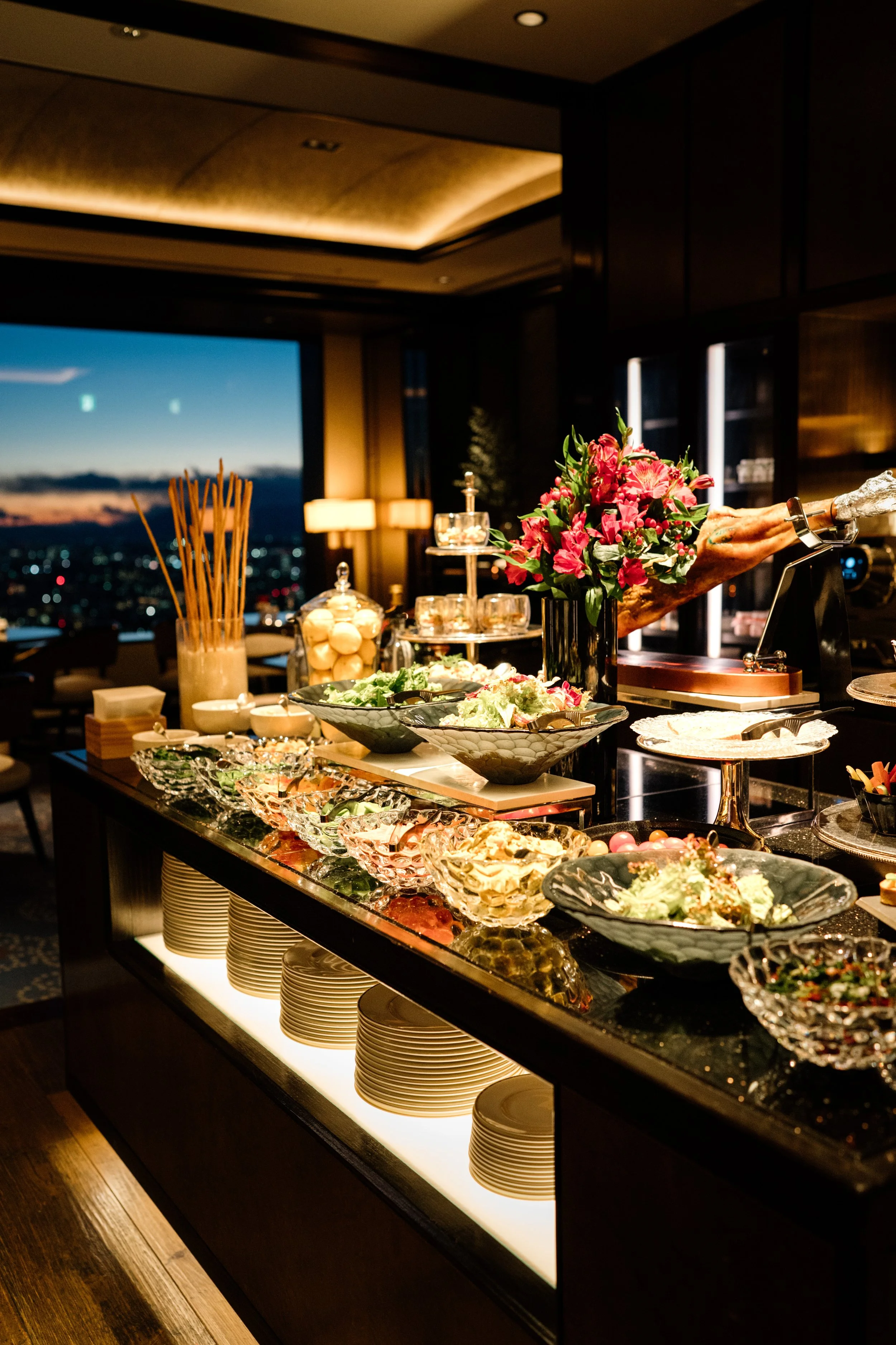 A buffet table with various salads, decorative bowls, and a bouquet of pink and red flowers at The Ritz-Carlton, Tokyo. Editorial hotel photography, Japan.