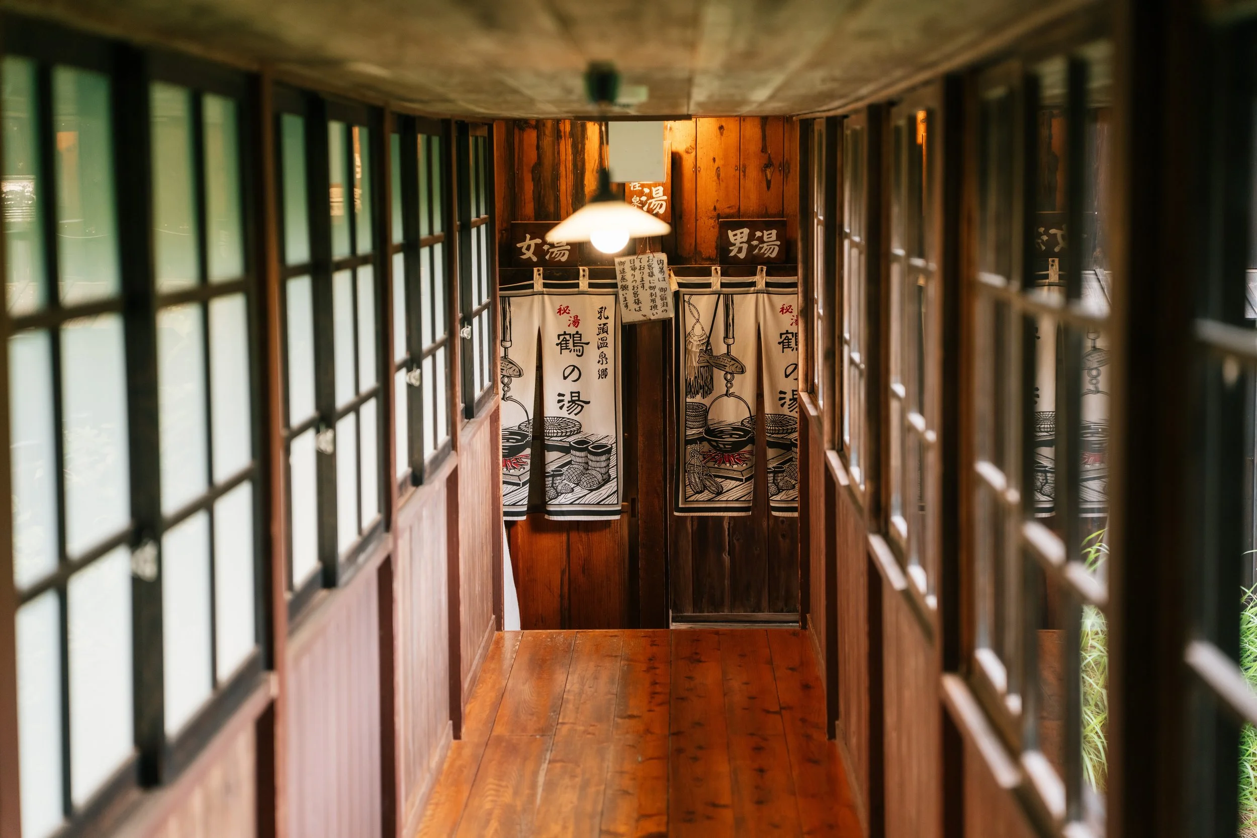 Traditional wooden hallway leading to a bathhouse entrance in Tsurunoyu Ryokan, Nyuto Onsen, with noren doors for separate men's and women's bath areas, travel photography, Japan.