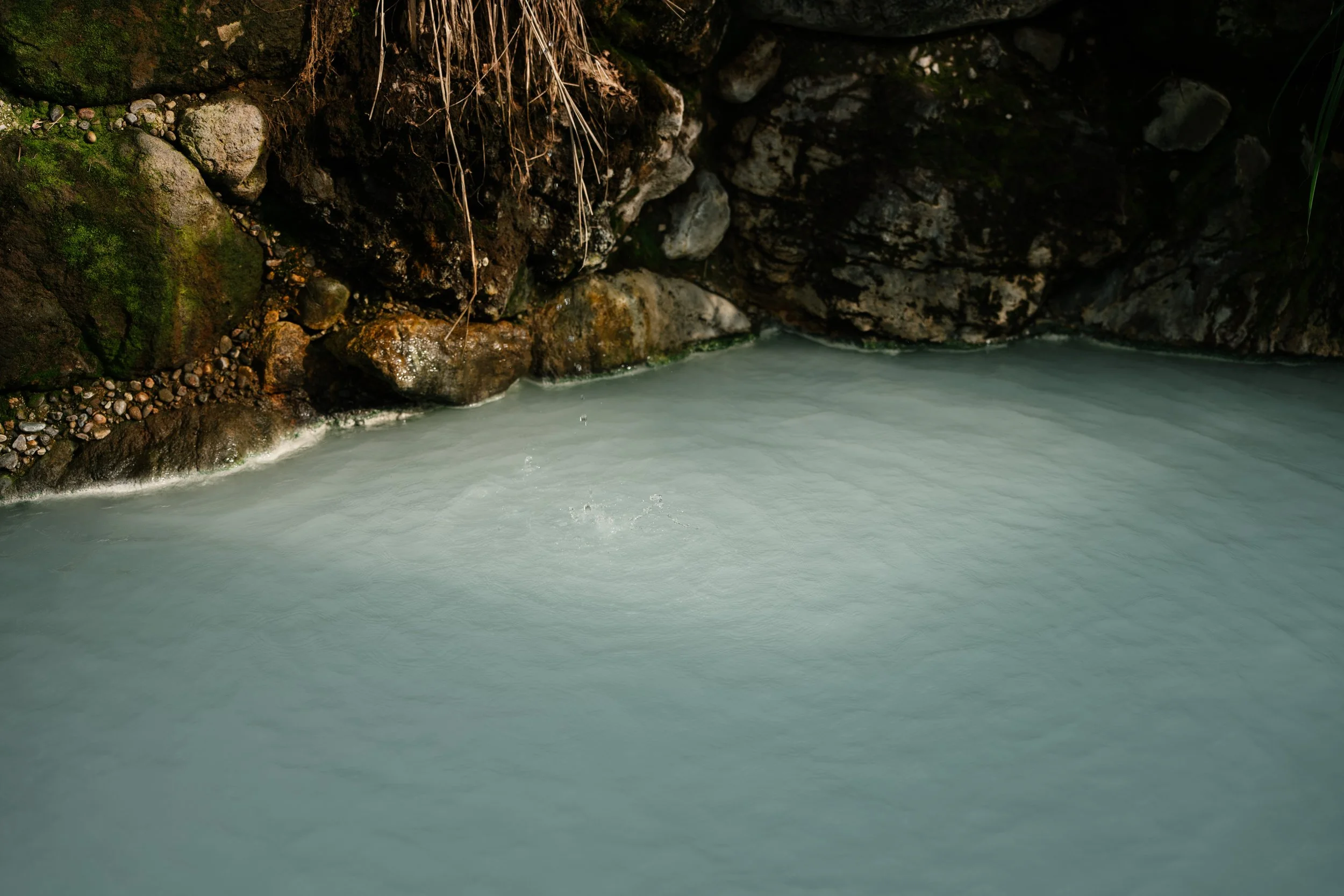 A view inside a rocky cave with moss on the rocks and water flowing at the bottom.