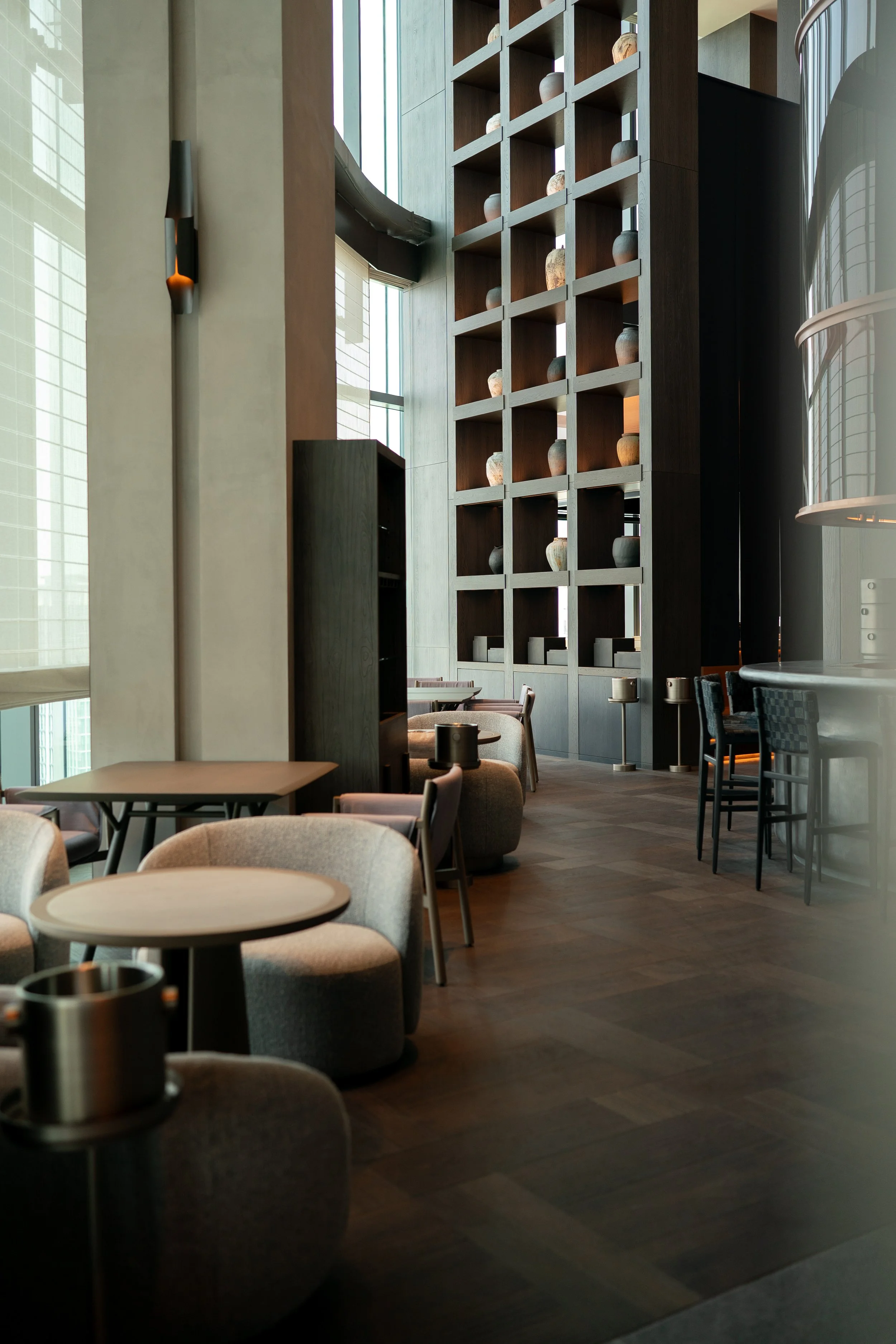 Interior of a modern restaurant or cafe with round tables, cushioned chairs, and a tall wooden shelving unit displaying decorative pottery at JW Marriott Tokyo hotel, editorial hospitality photography, Japan.