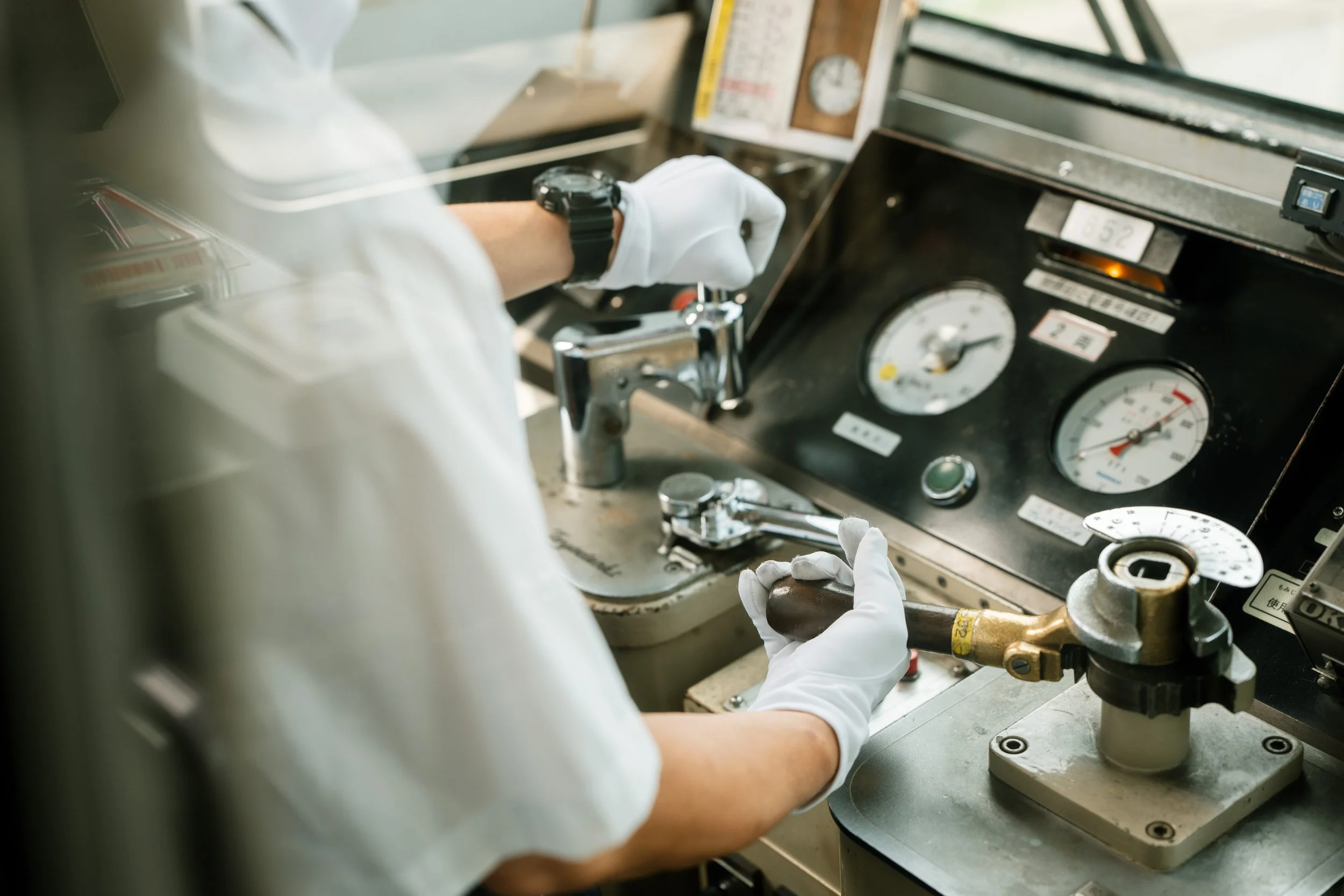 Person wearing white gloves working with machinery, adjusting a valve, with gauges and control panels around.
