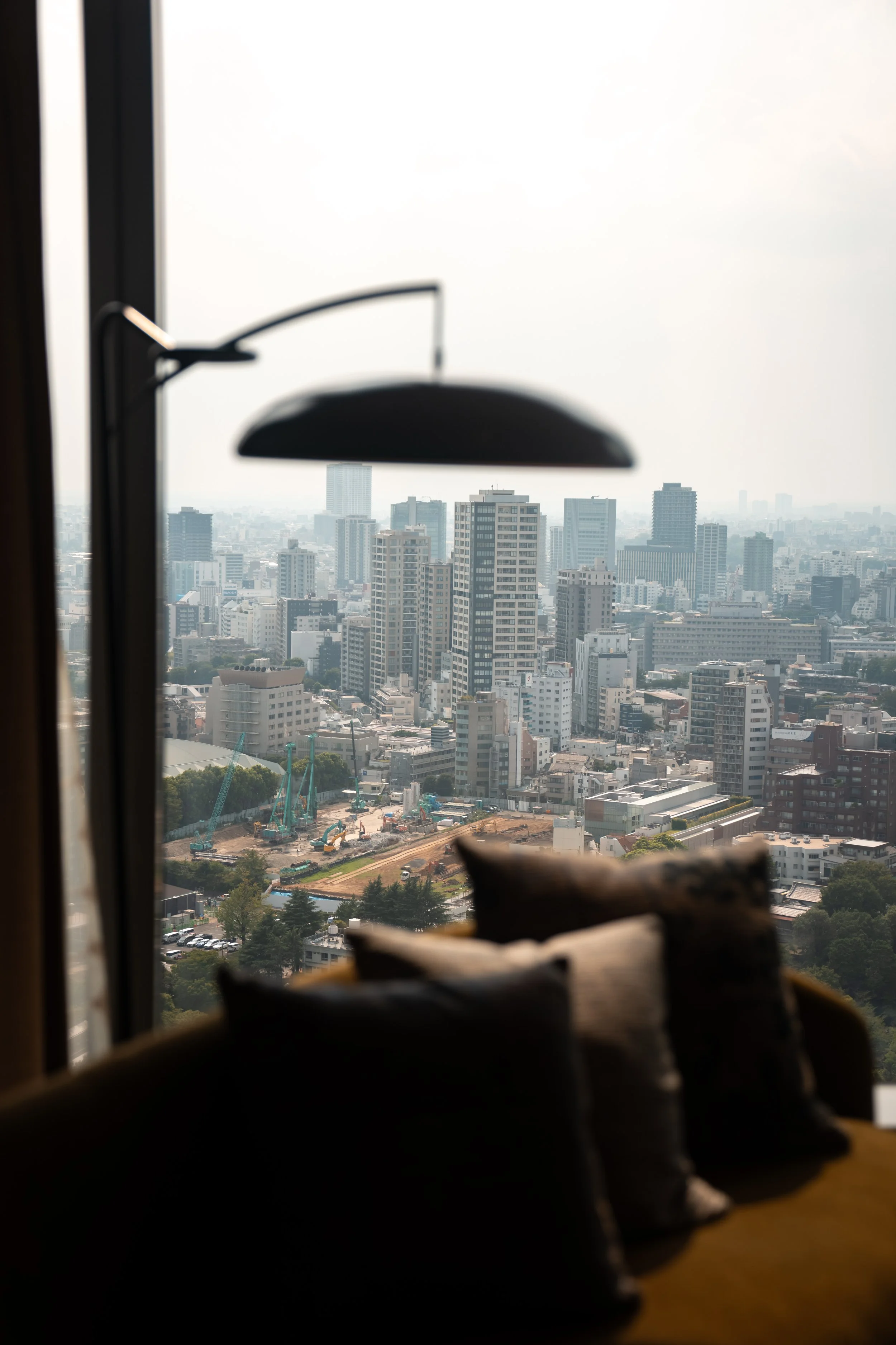 View of city skyline with tall buildings through a window, with an out-of-focus lamp in the foreground.