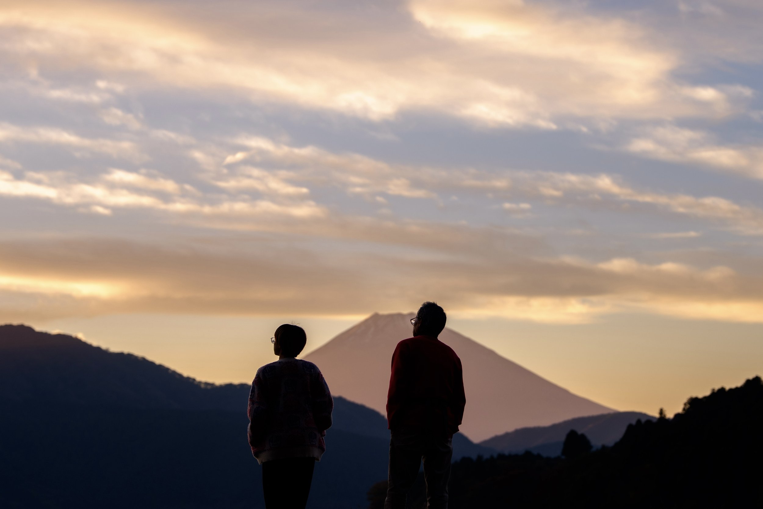 Two people standing outdoors at sunset overlooking Mount Fuji, travel photography in Japan.