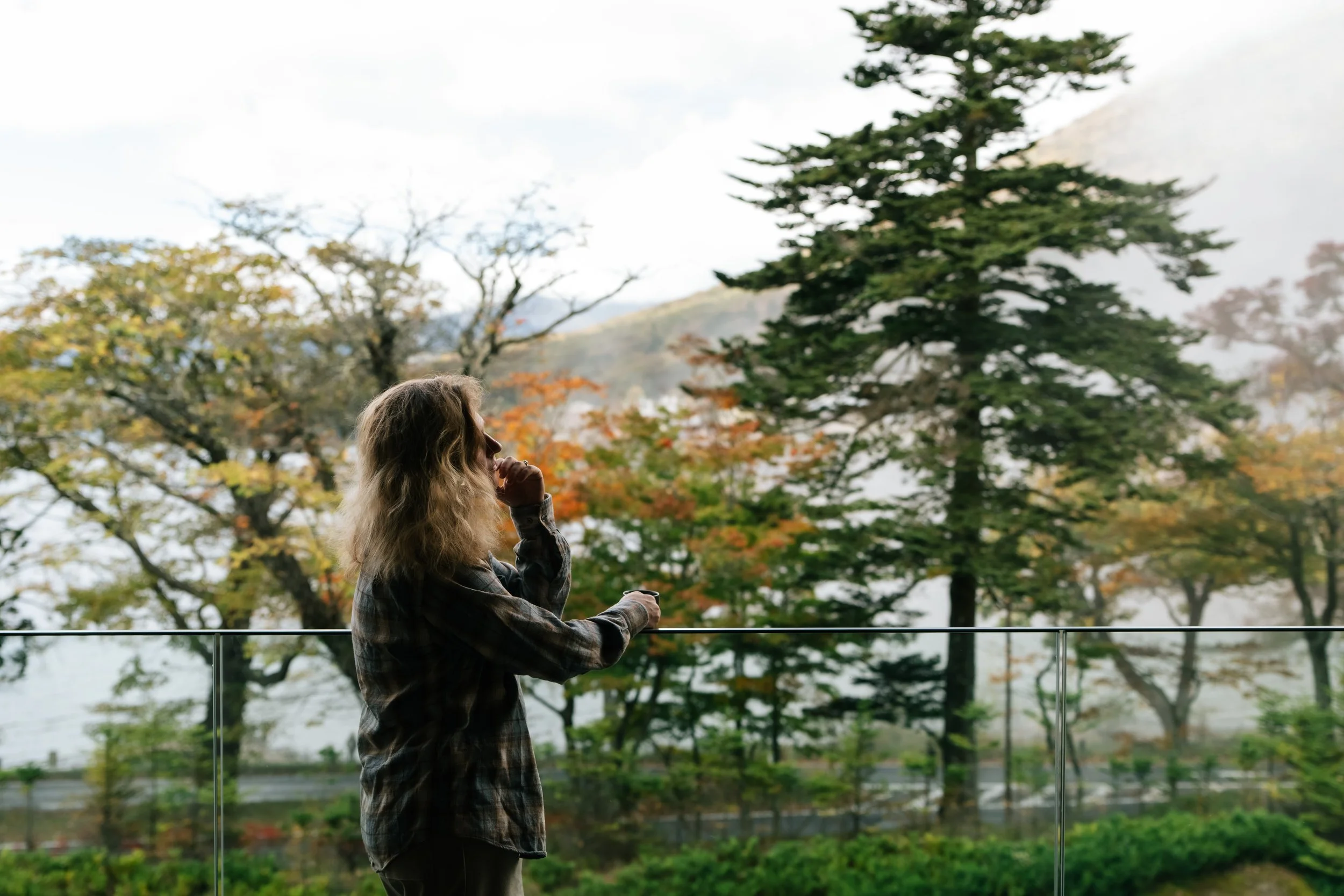 A woman with long, wavy hair standing outdoors with trees in autumn colours in the background during an editorial photography session in Nikko, Japan.