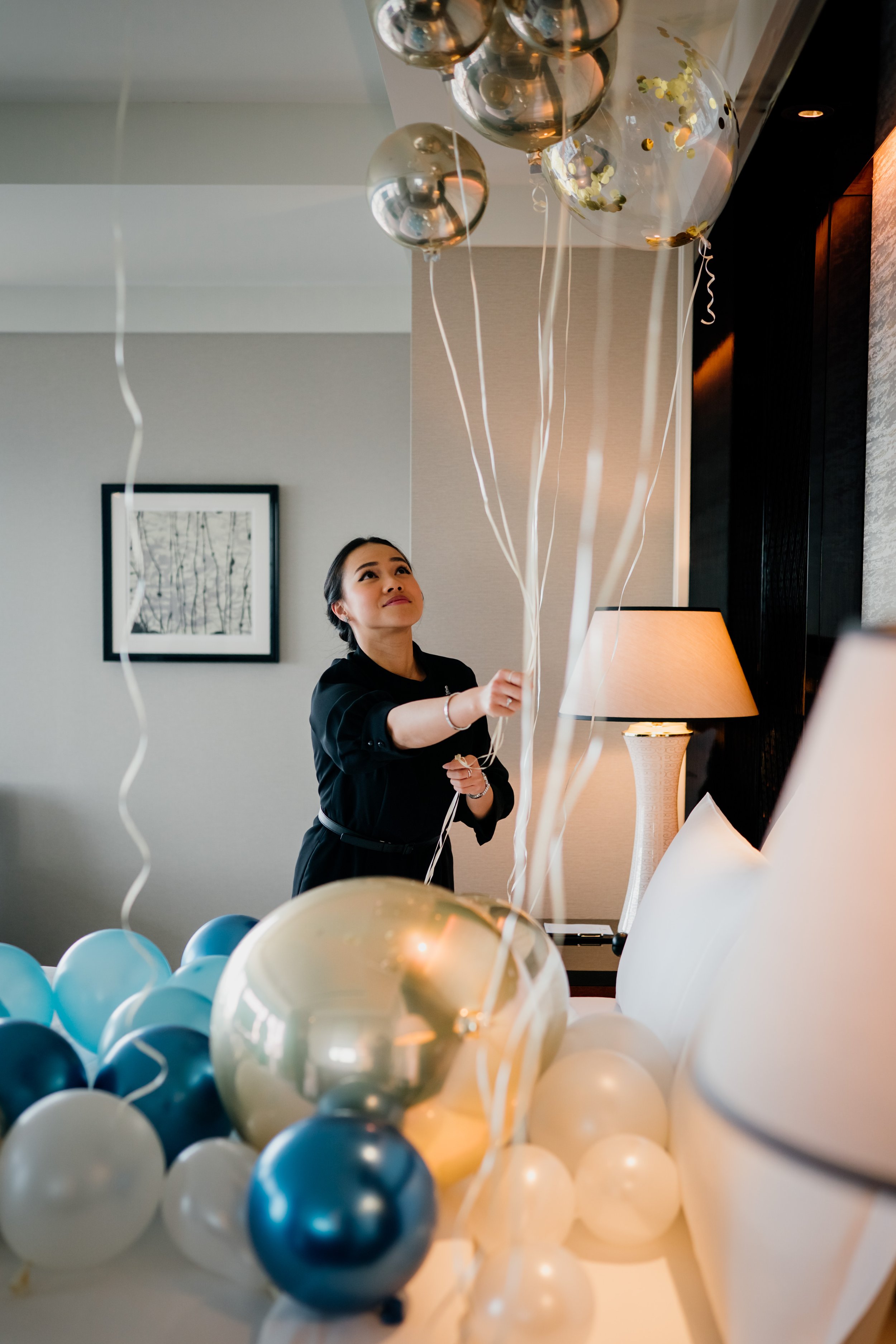 A guest enjoying a celebration standing behind a large arrangement of blue, white, and gold balloons at The Ritz-Carlton, Tokyo. Editorial hospitality photography, Japan.  
