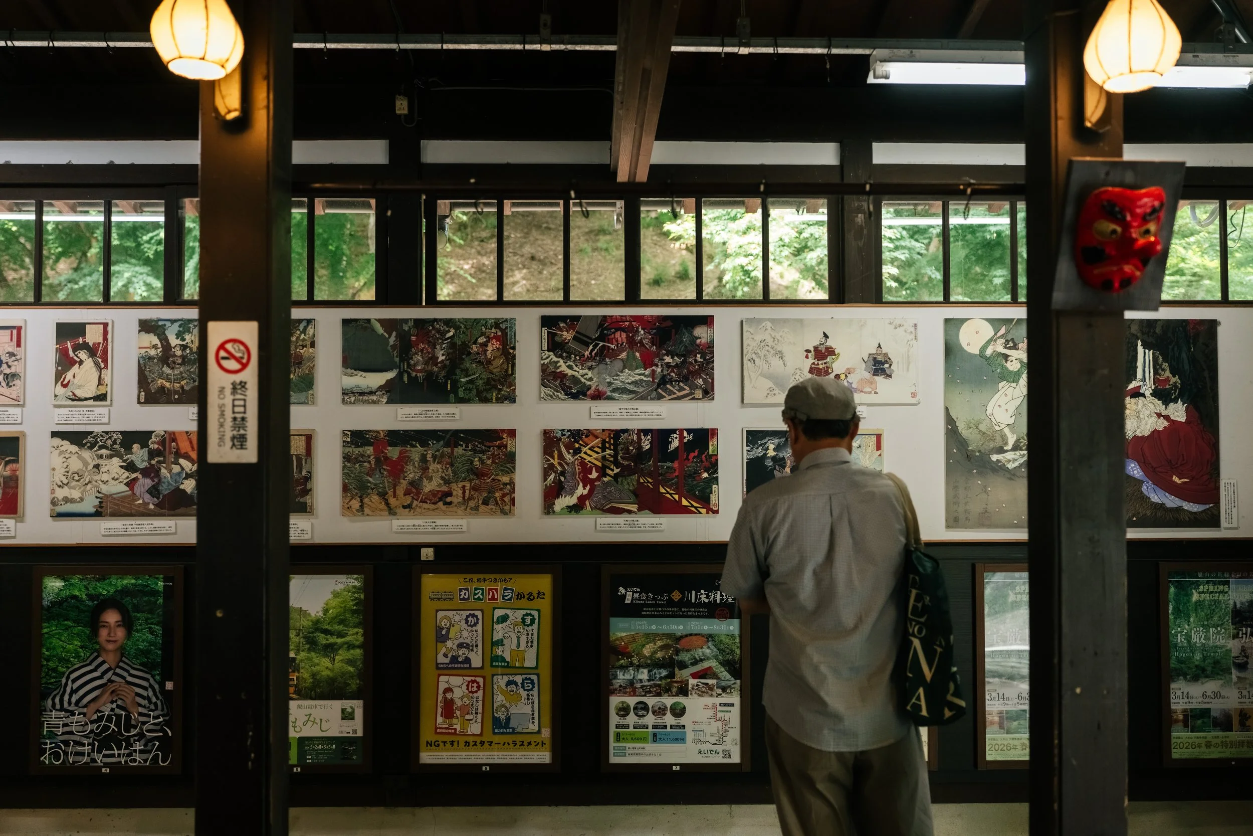 People viewing artwork and posters in an indoor gallery with large windows and greenery outside.