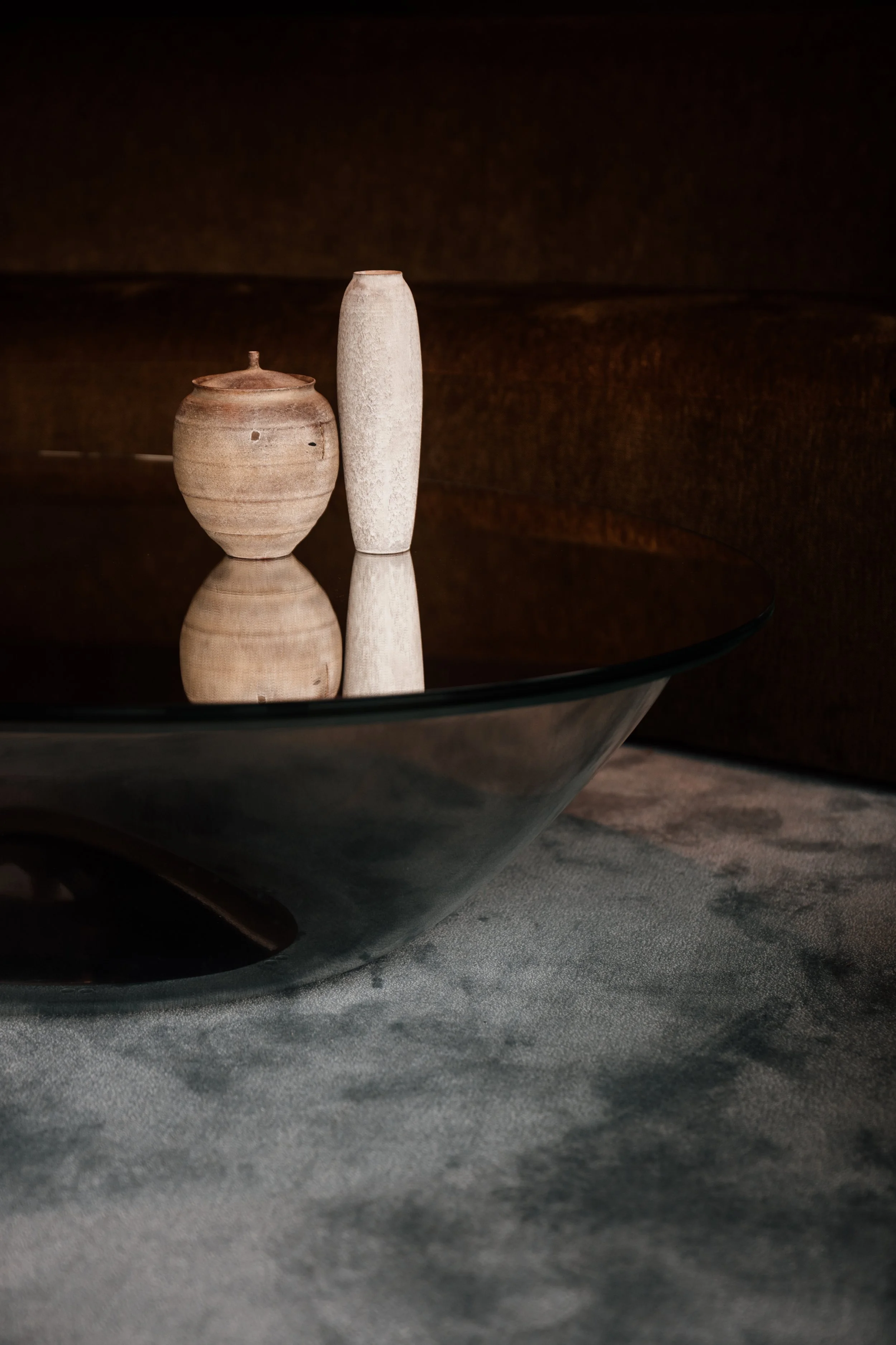 Two ceramic vases, one round with a lid and small handle, and one tall and narrow, placed on a reflective black surface with a dark background at JW Marriott hotel, editorial hotel photography, Japan.