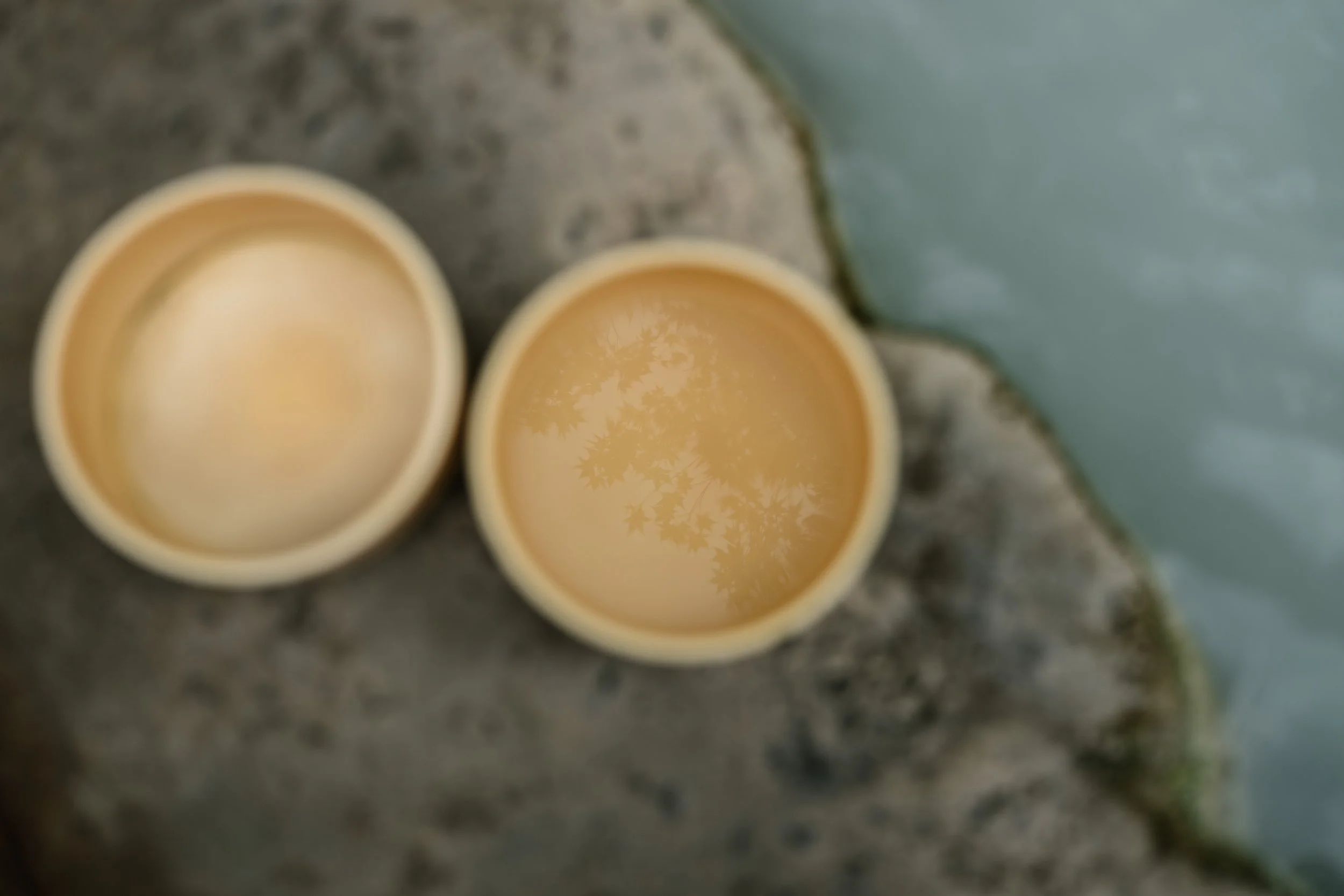 Two beige cups filled with a light-colored beverage, placed on a stone surface near a body of water.