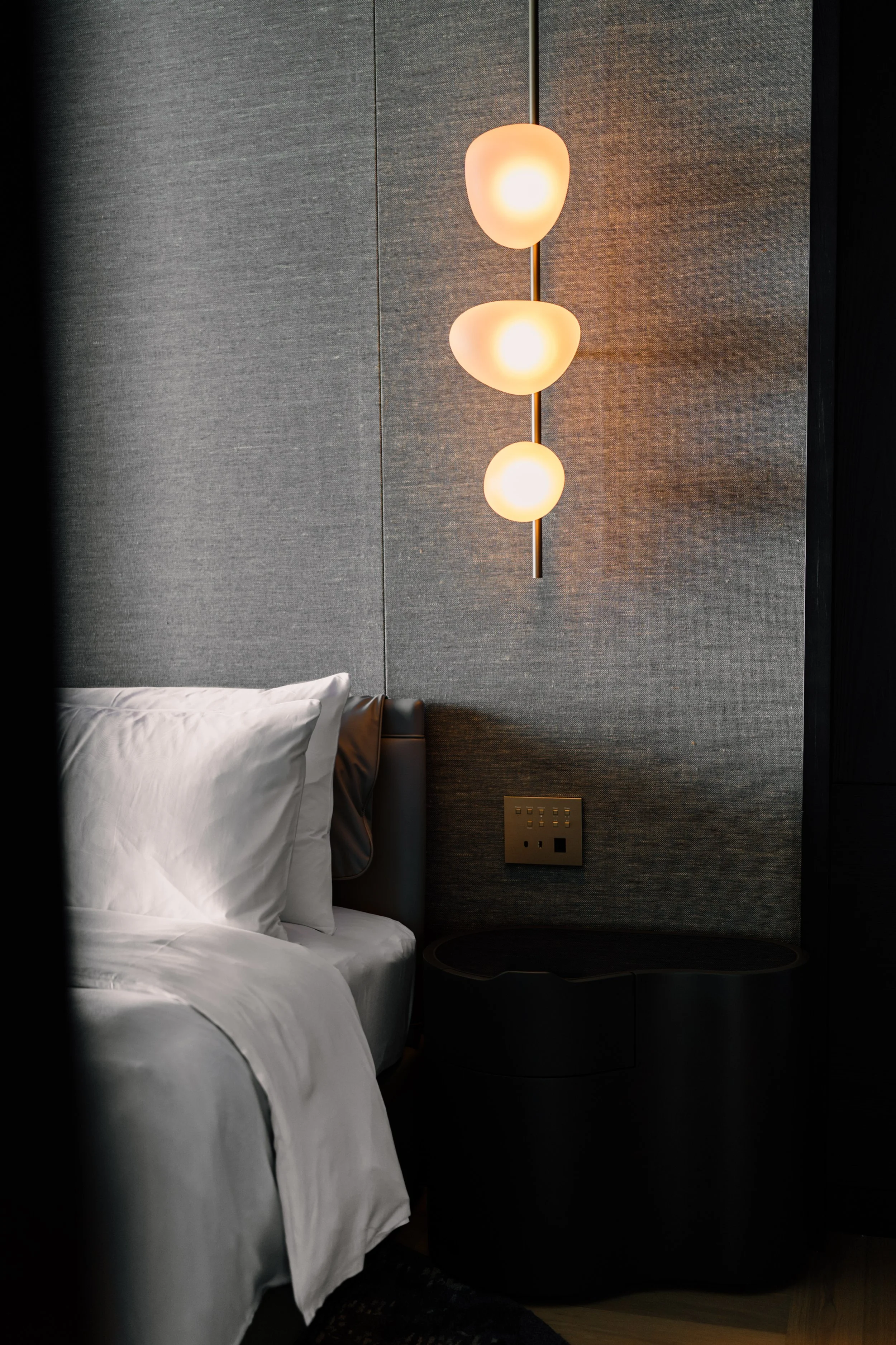 Close-up of a modern bedroom with a bed, white bedding, gray headboard, wall-mounted lamp, and electrical outlets at JW Marriott Tokyo hotel, editorial hotel photography, Japan.