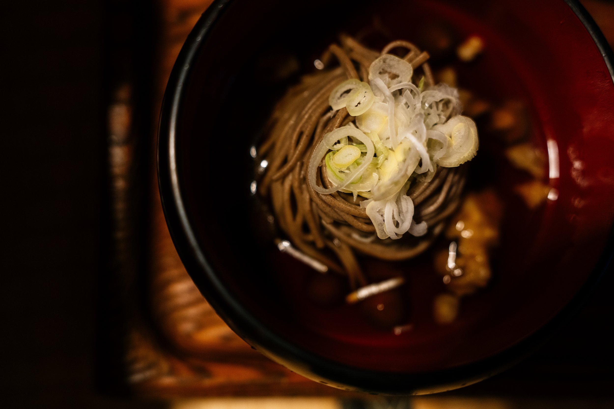 Close-up of a black cup filled with soba noodles topped with sliced green onions