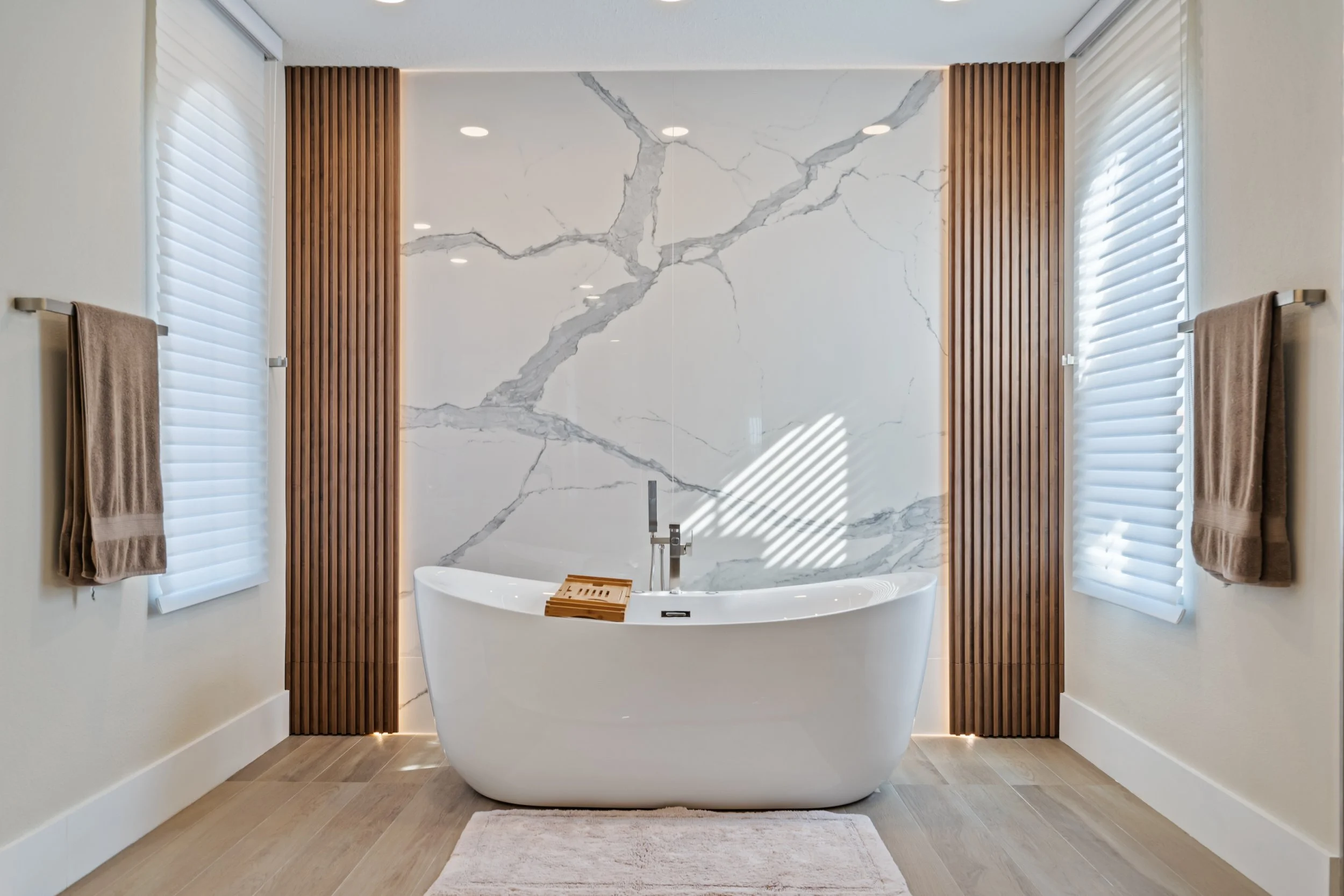 Modern bathroom design with a freestanding bathtub, marble feature wall, warm wood accents and natural finishes.