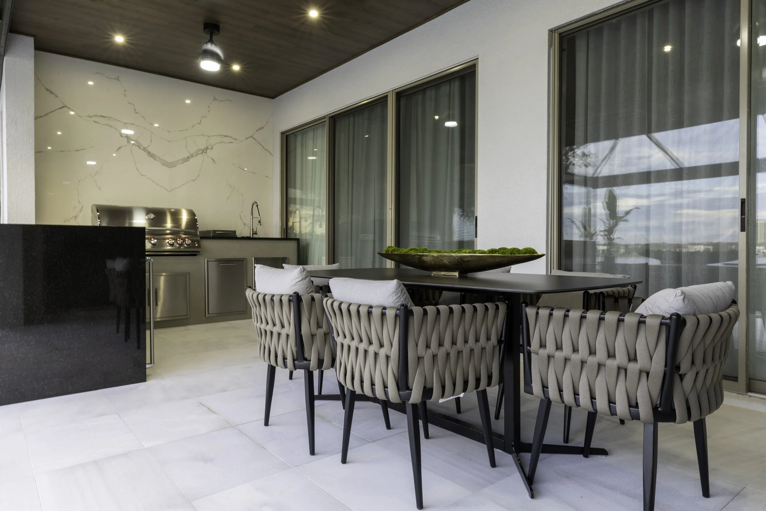 Contemporary outdoor kitchen and dining area with custom cabinetry, stone finishes, grill and covered entertaining space.