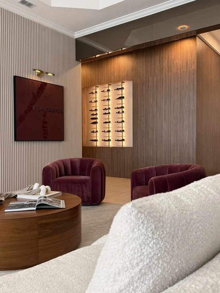 Contemporary living room with velvet armchairs, textured feature wall, custom wine display and warm ambient lighting.