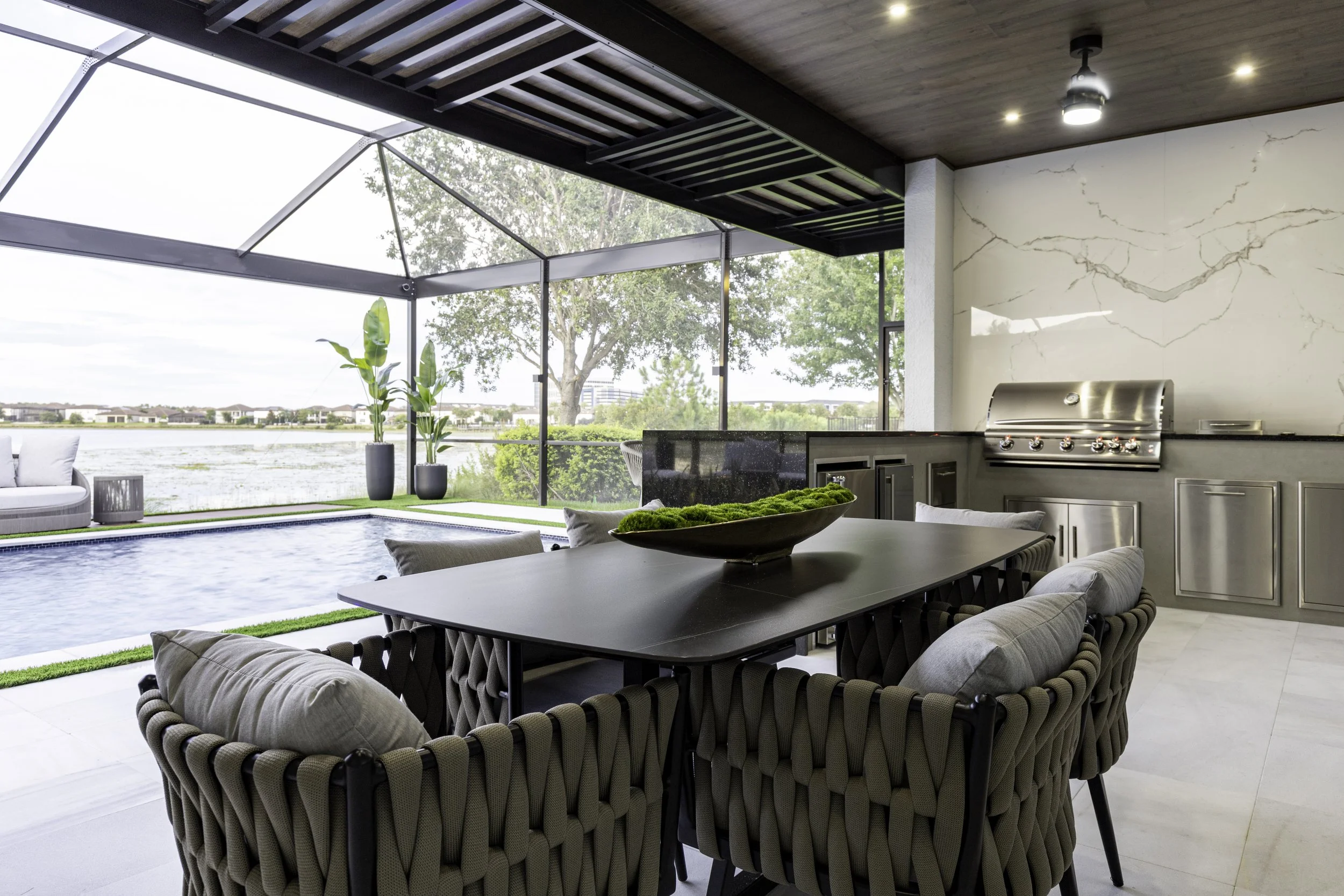Outdoor living area with swimming pool, covered dining space, tropical landscaping and waterfront views.