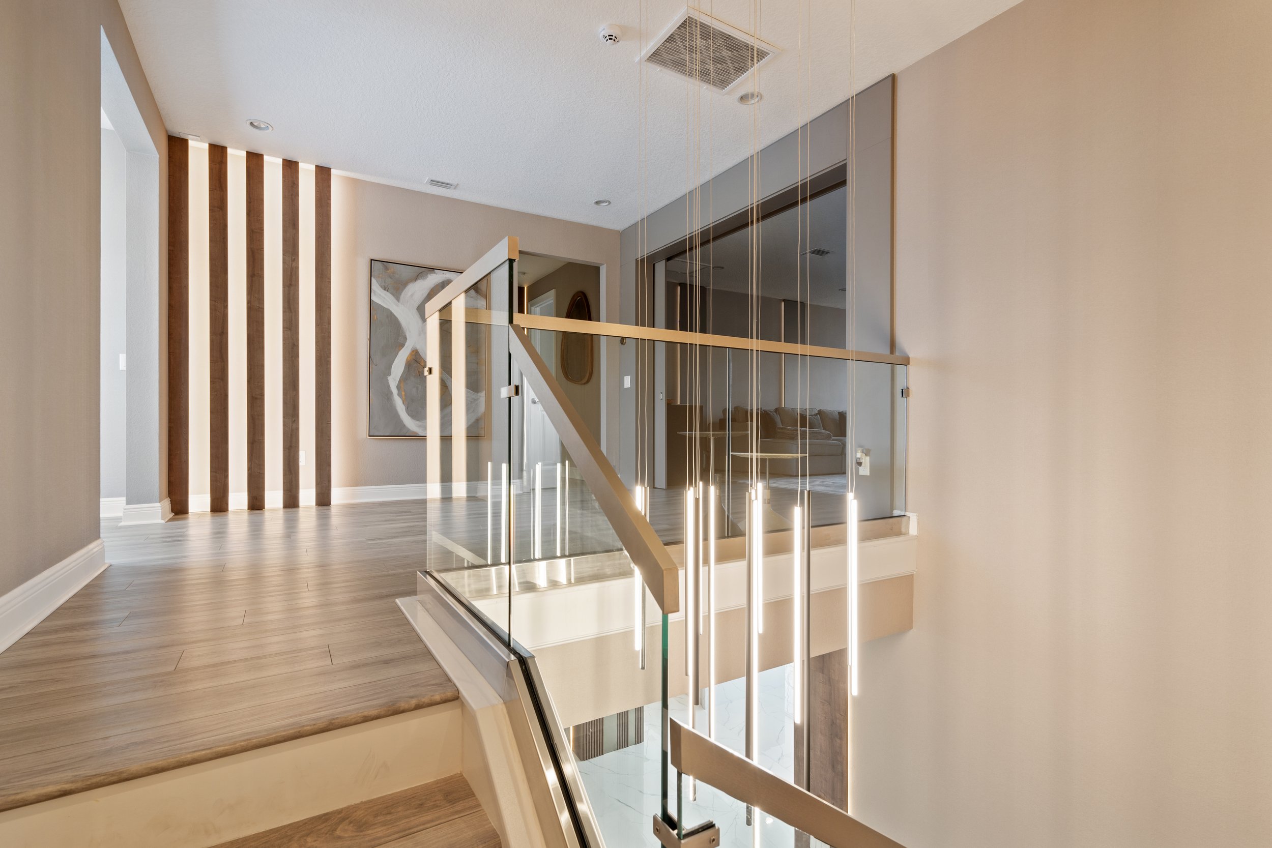 Contemporary staircase design with glass railing, light wood flooring, vertical wood slat wall and modern pendant lighting.