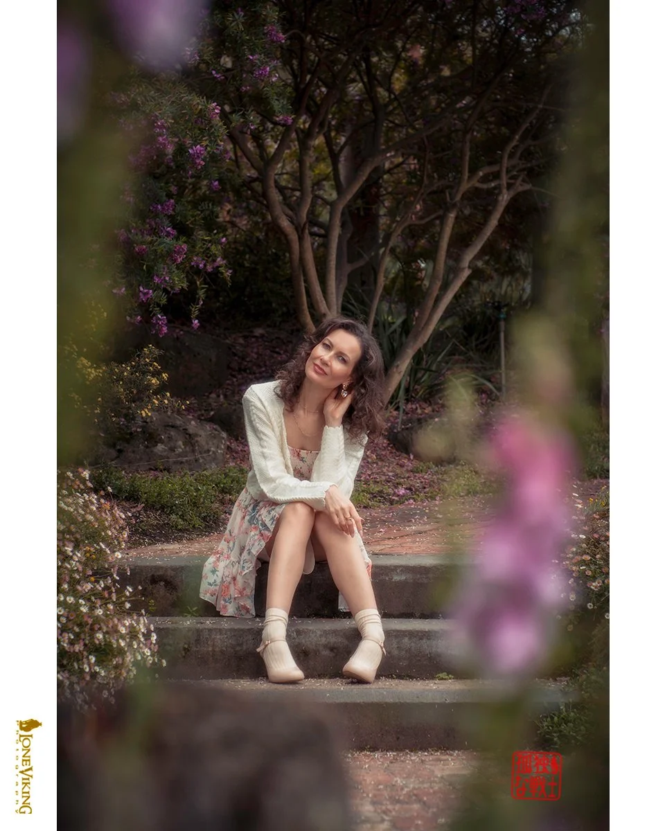 A woman sitting on outdoor steps surrounded by flowers and trees