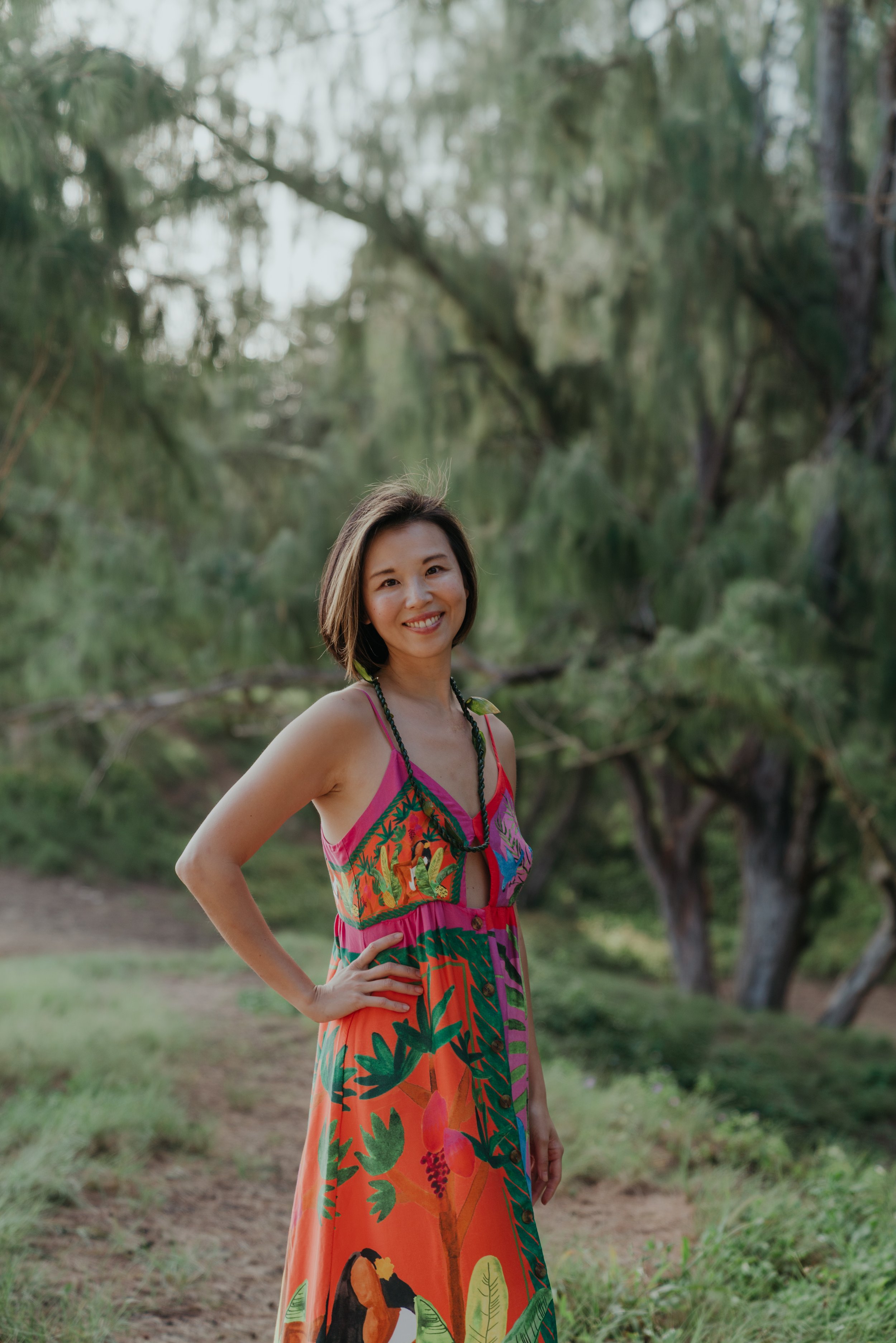 A woman with short brown hair smiling and wearing a colorful tropical dress with a jungle background.