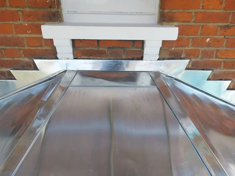 A shiny metal rooftop attached to a brick wall exterior.