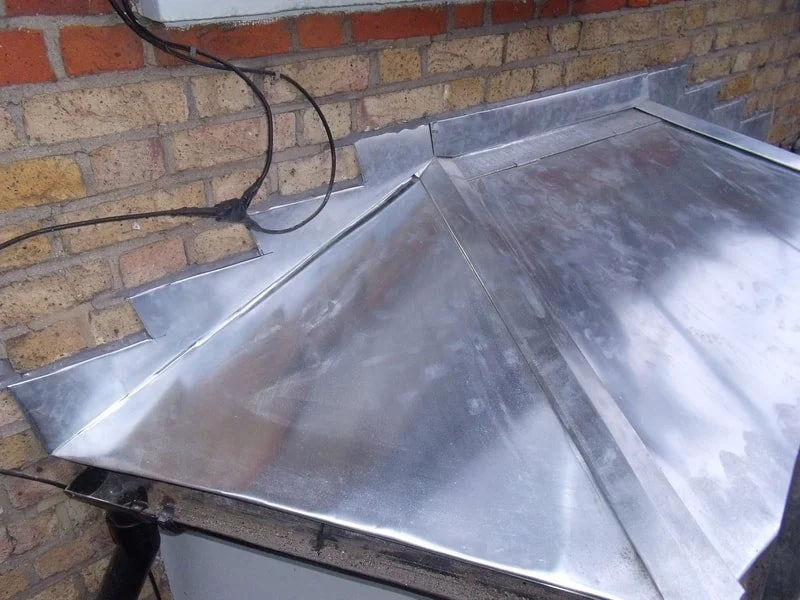 Close-up of a metal roofing gutter and flashing installed against a brick wall.