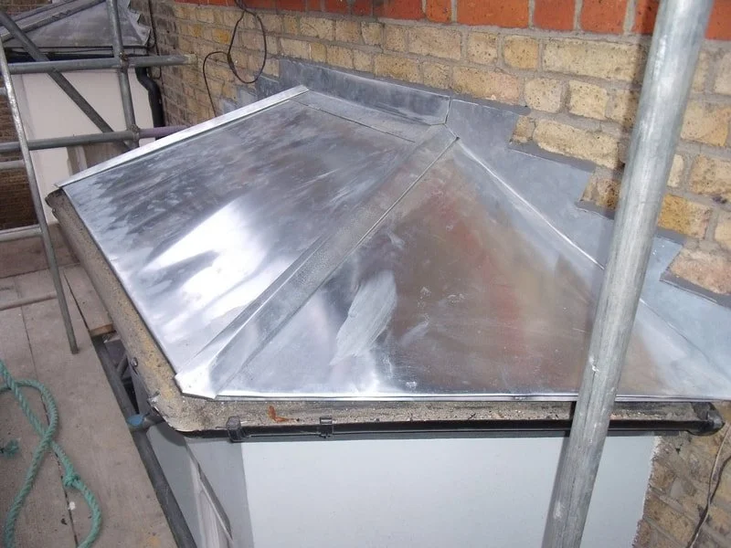 Metal roofing sheet on a construction site with scaffolding and a brick wall in the background.