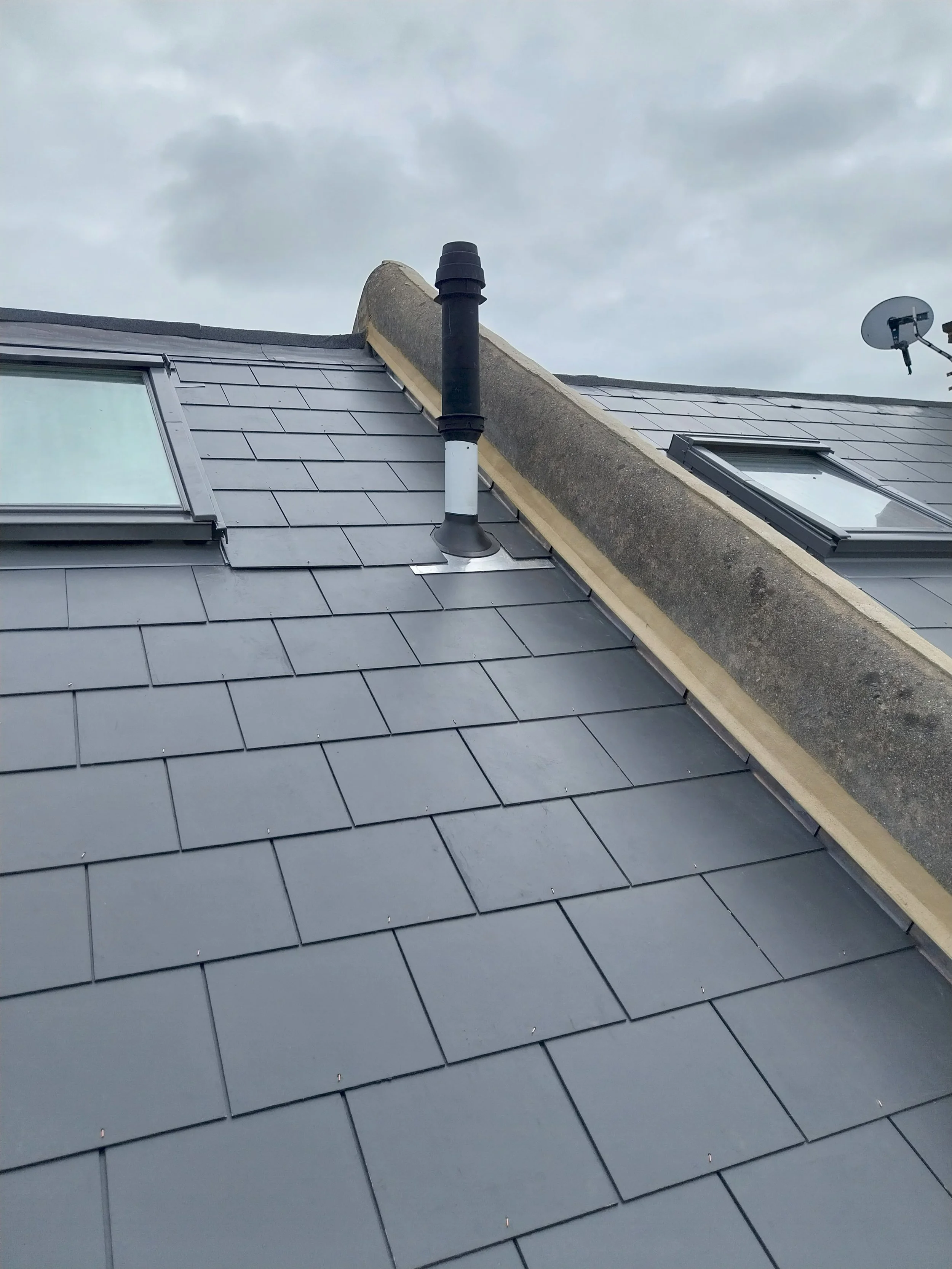 Roof with slate tiles, a skylight window, a black vent pipe.