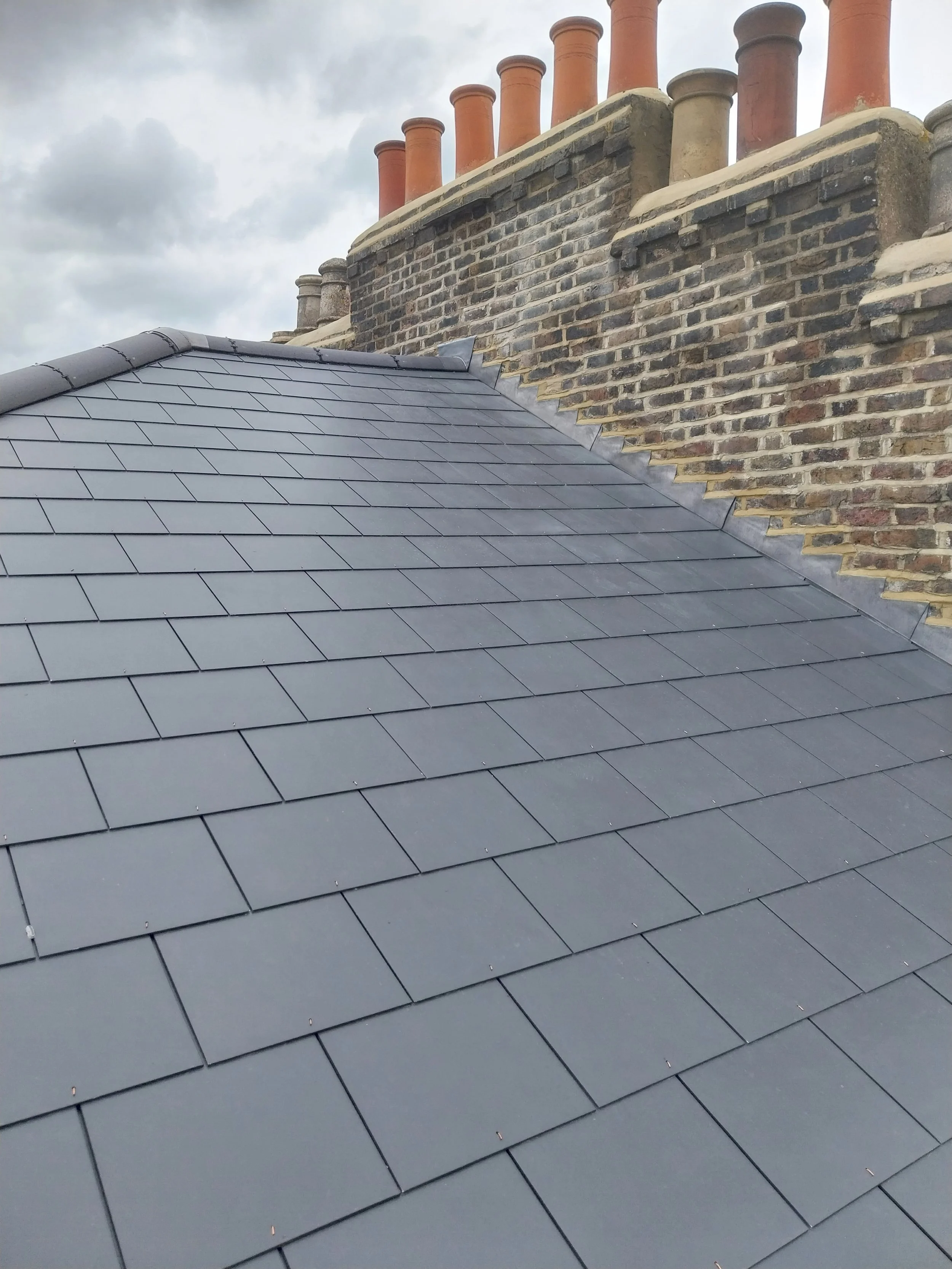 Rooftop with dark gray tiles and a brick chimney.