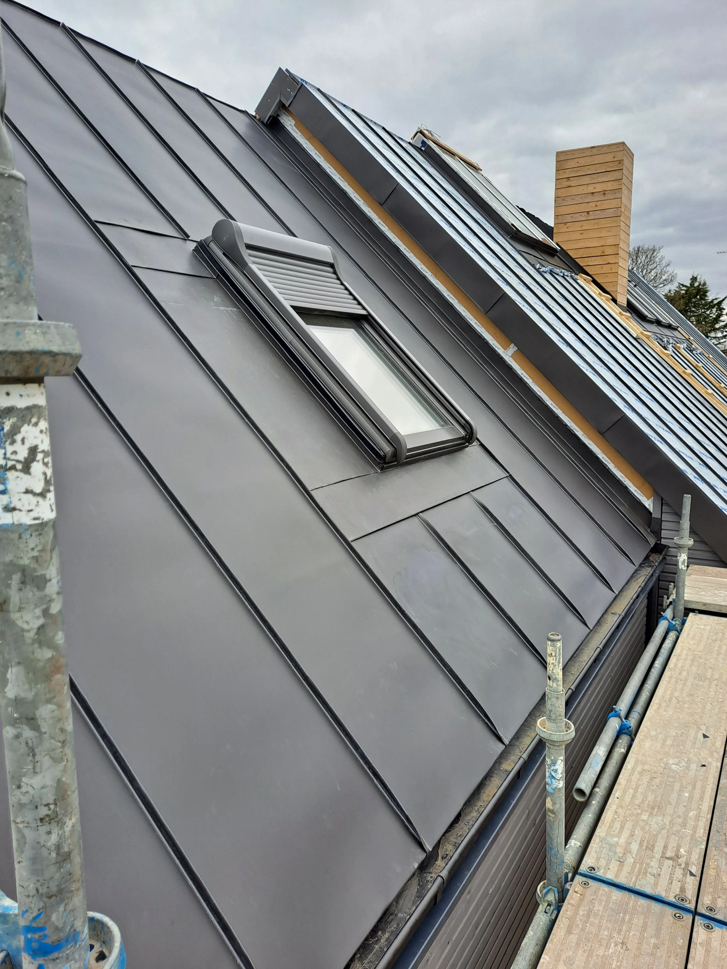 A metal roof with solar panels and a skylight, construction scaffolding and wooden planks. 