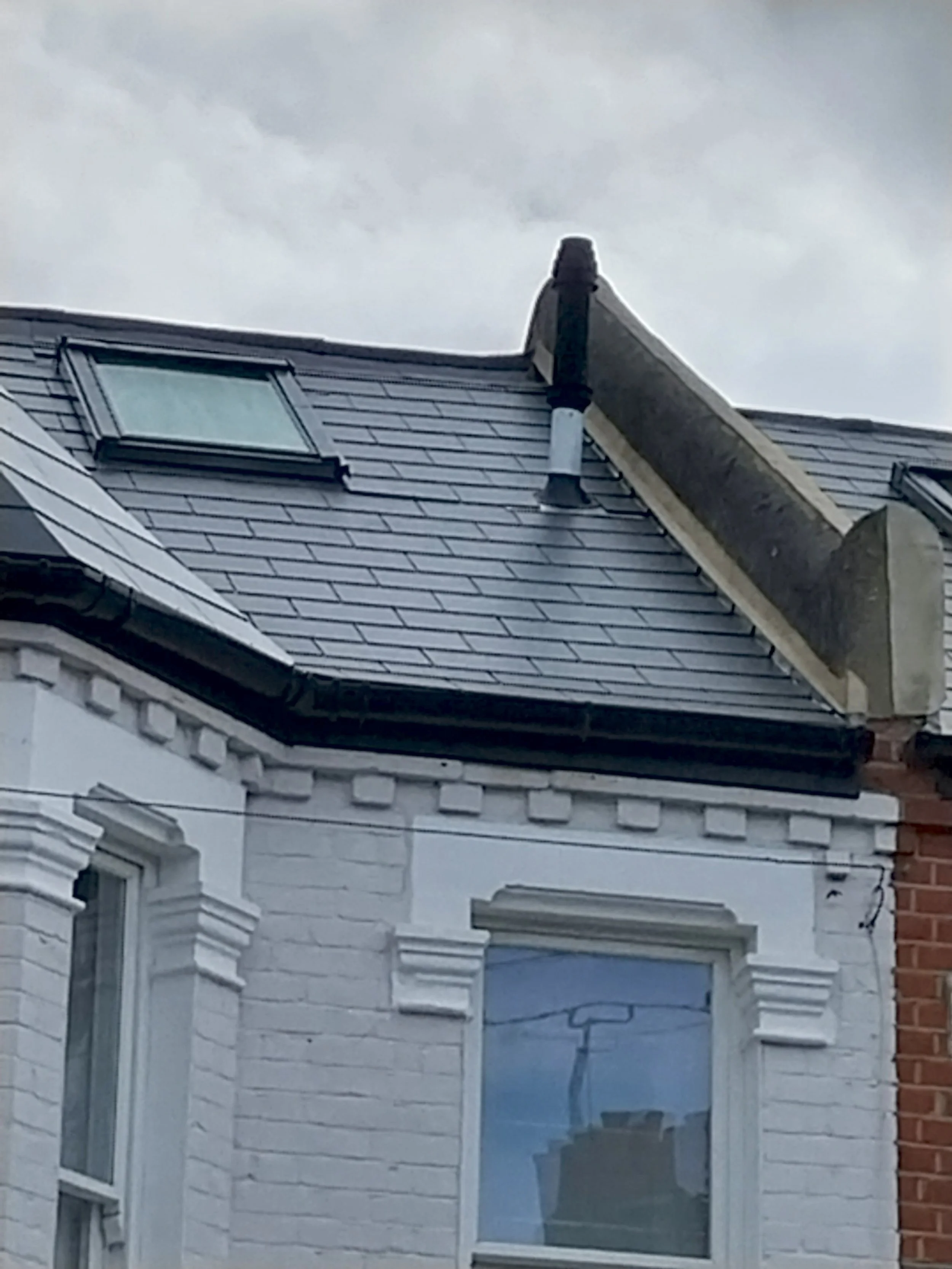 Close-up of the upper story of a white brick house with a skylight and part of a dormer window.