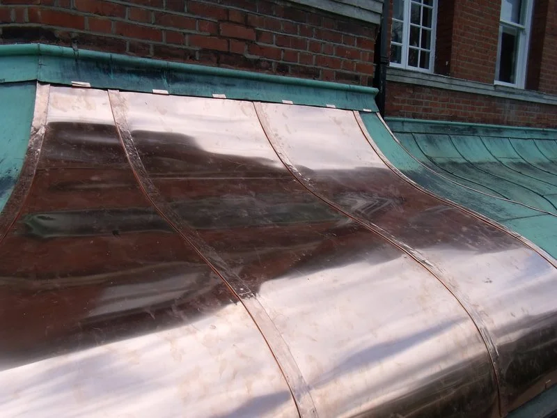 Copper roof with a curved design, partially visible brick building with windows.