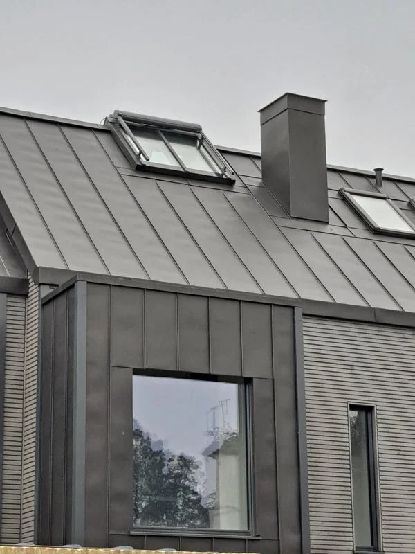Close-up of VMZINC Anthra (standing seam) roof and façade cladding, modern house roof with gray metal panels, skylights, and a chimney.