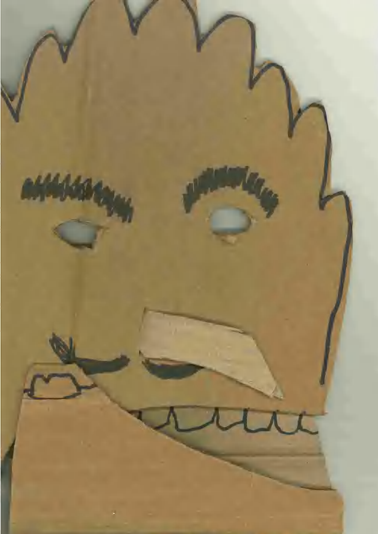 A paper craft of a smiling face with spiky hair, eyebrows, and eyes drawn with black marker. The face is made from cut-out brown paper with black outlines for the hair and facial features.