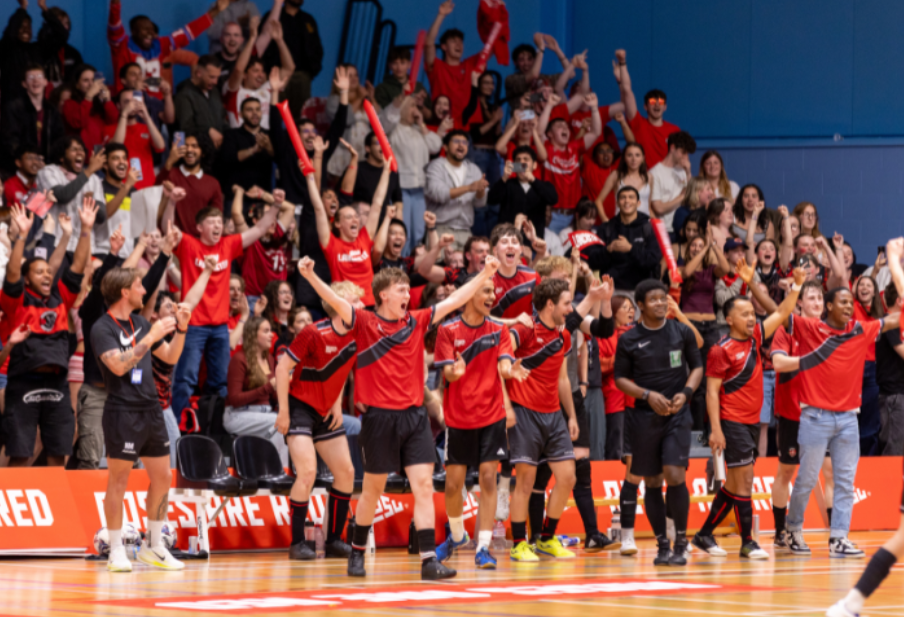 A group of athletes in red celebrating on a sports court while spectators cheer at Roses.