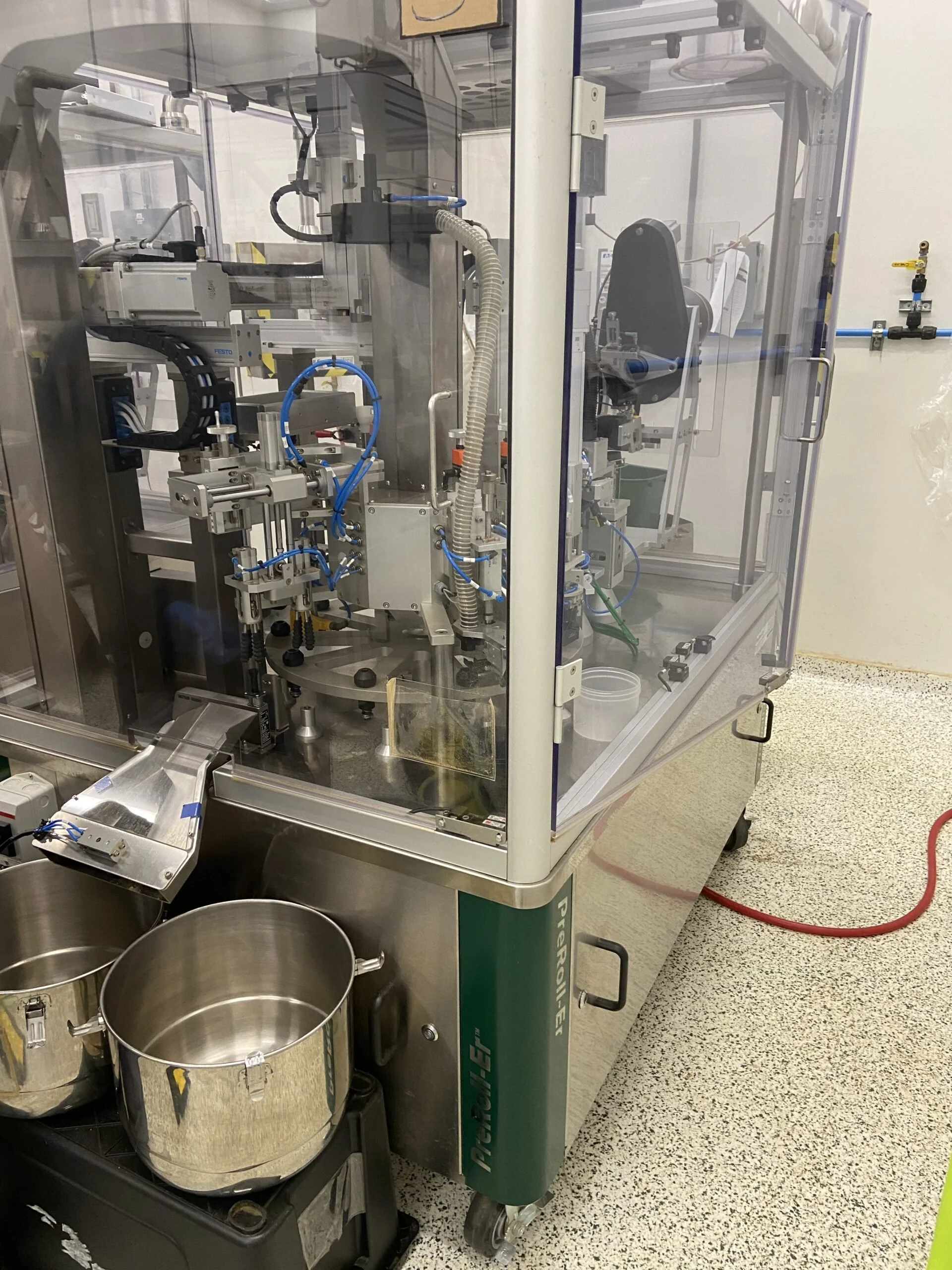 An enclosed preroll automation machine with visible internal mechanisms in a production room.