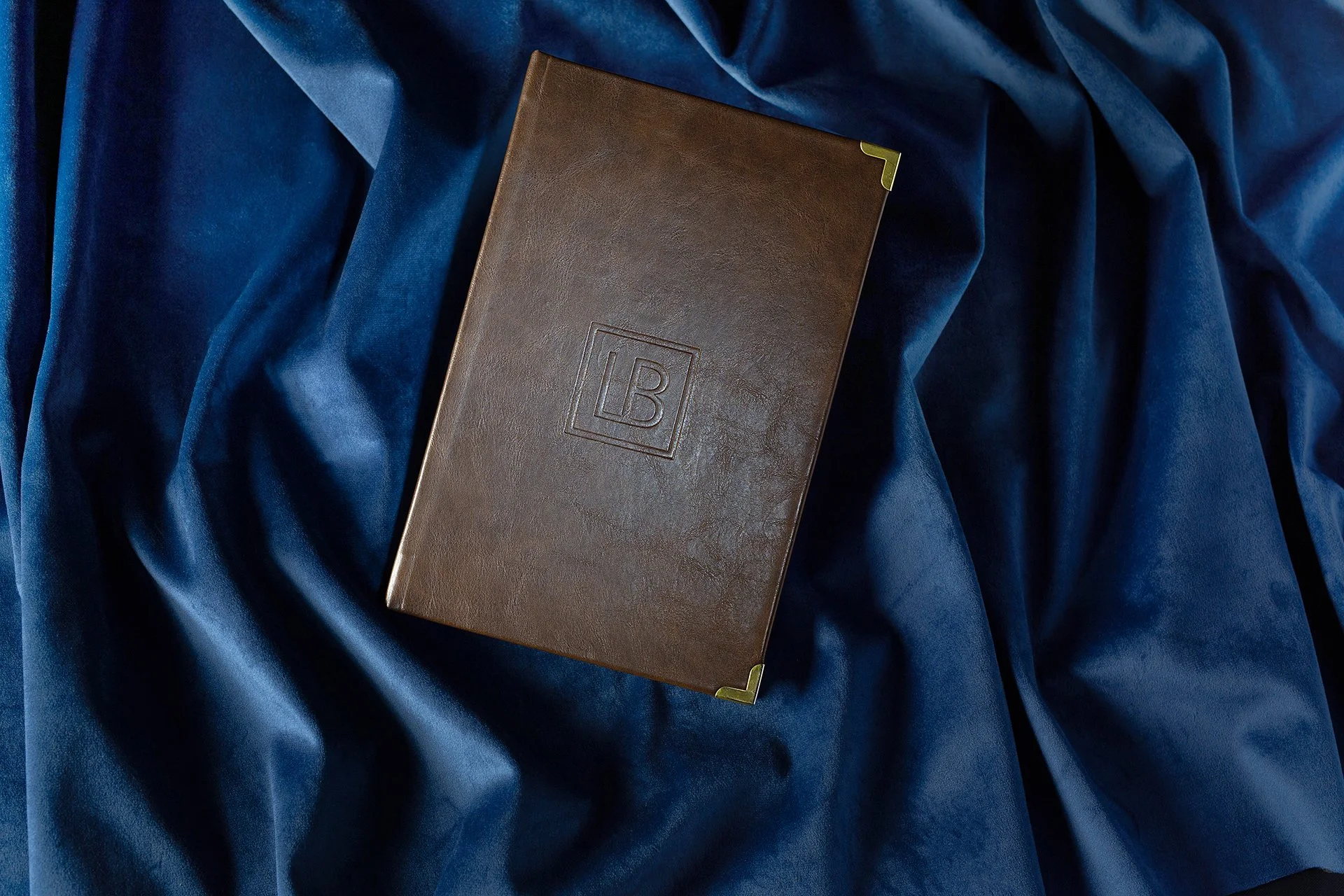 A brown camel leather cocktail menu cover, a 16-page cocktail menu was created for Library Bar, a concept bar within the Edition Hotels group, inspired by the atmosphere of an old library.