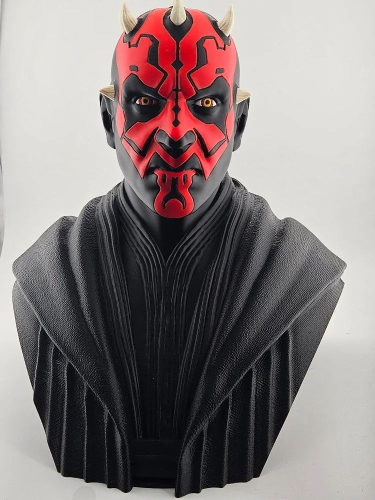 Bust of Darth Maul with red and black face paint, yellow eyes, and small horns, wearing black robes.