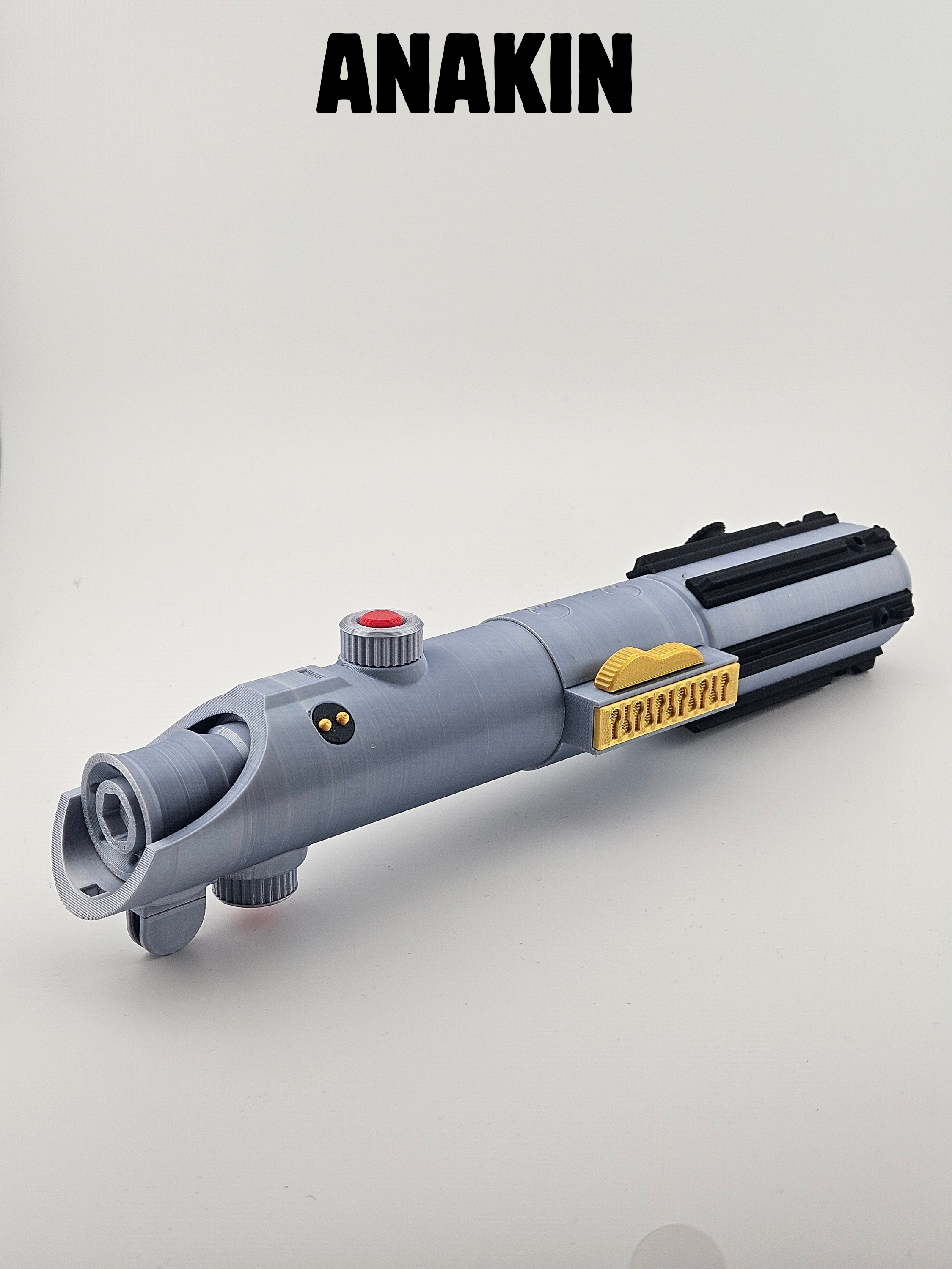 Toy lightsaber with a gray handle, black accents, a yellow details, and a red button, placed on a plain white background. The word "Anakin" is written in large black letters at the top.
