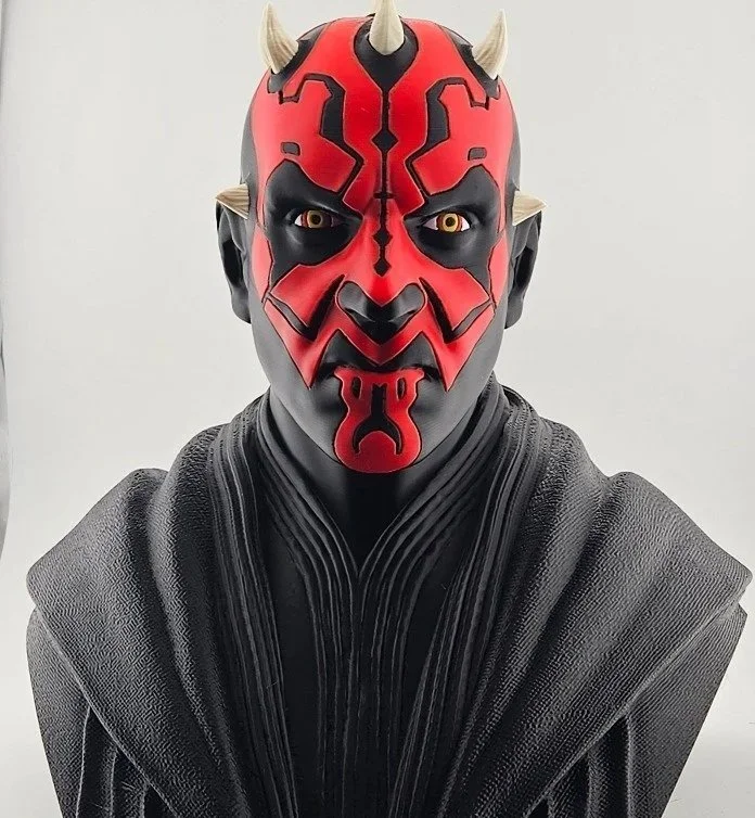 A detailed figure of Darth Maul from Star Wars with red and black face paint, yellow eyes, and small horns on his head, wearing a black textured cloak.