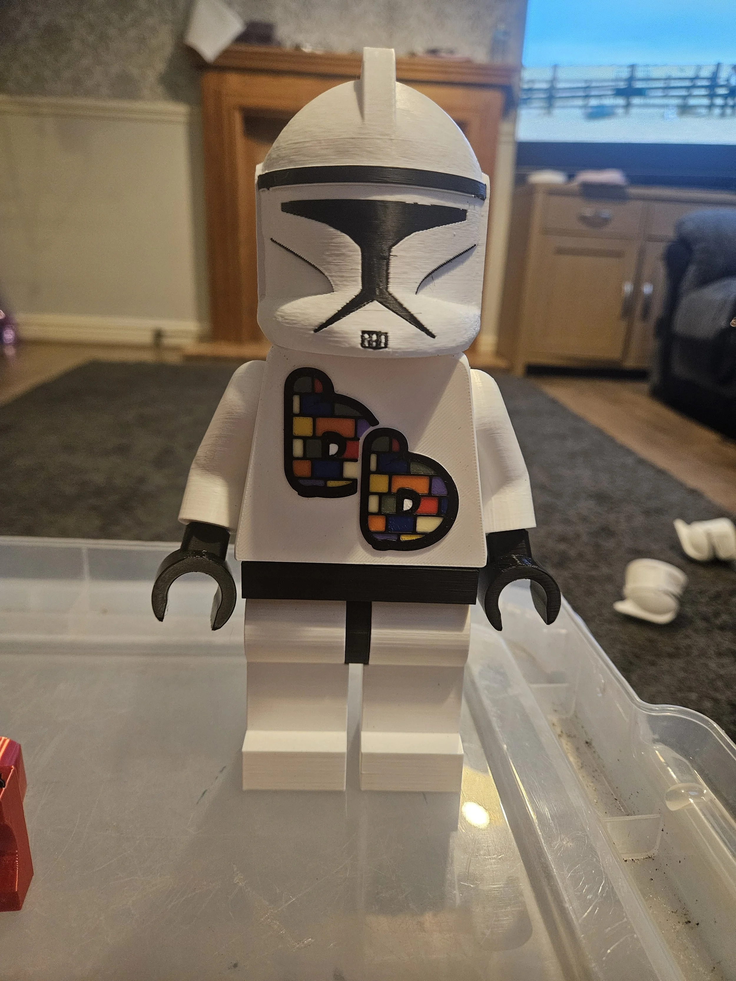 A LEGO Star Wars figure resembling a clone trooper, standing on a white platform with a backdrop of a living room with wooden furniture and a television.