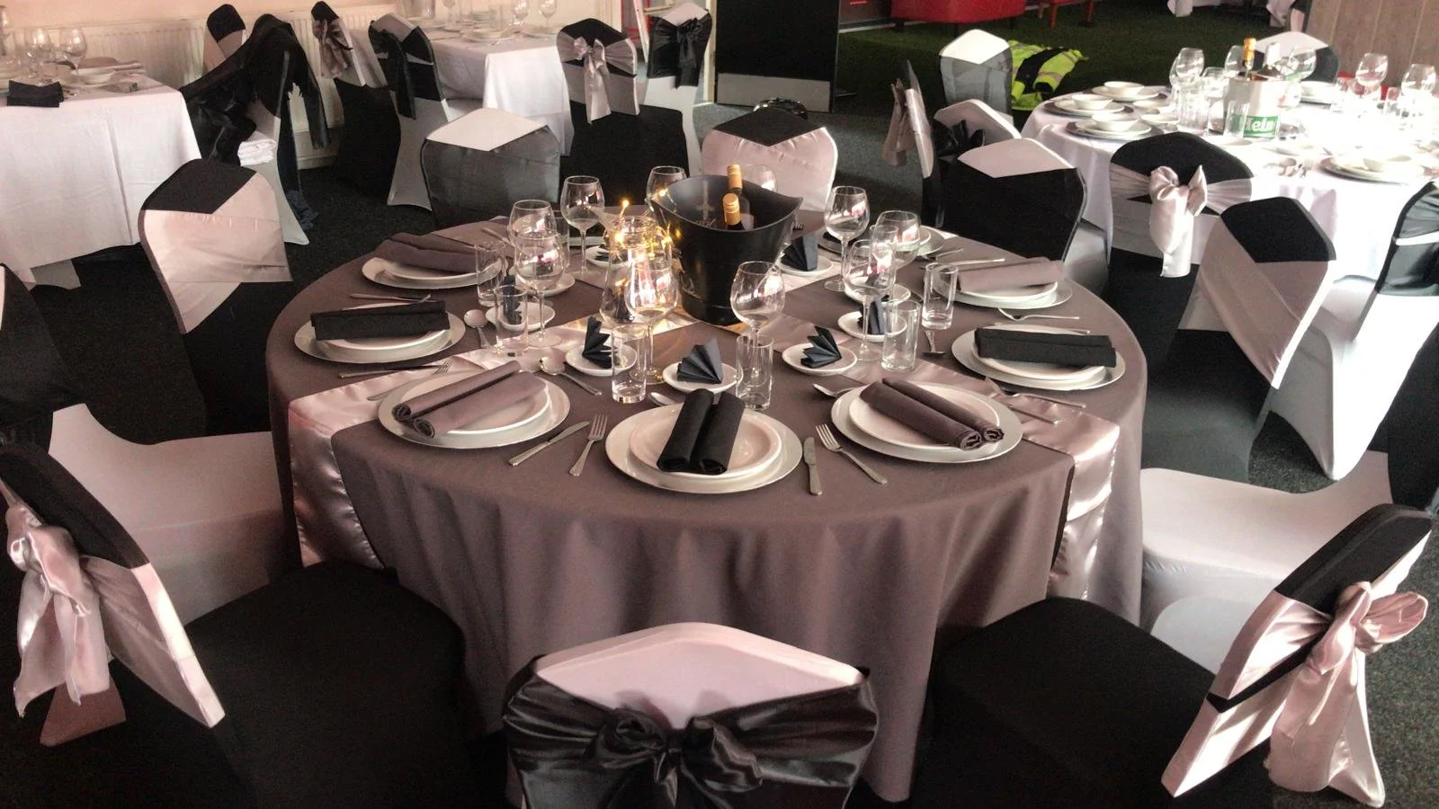 Round banquet table set for a formal event with black and white chair covers, black napkins, wine glasses, and a ice bucket with champagne bottles in the center.